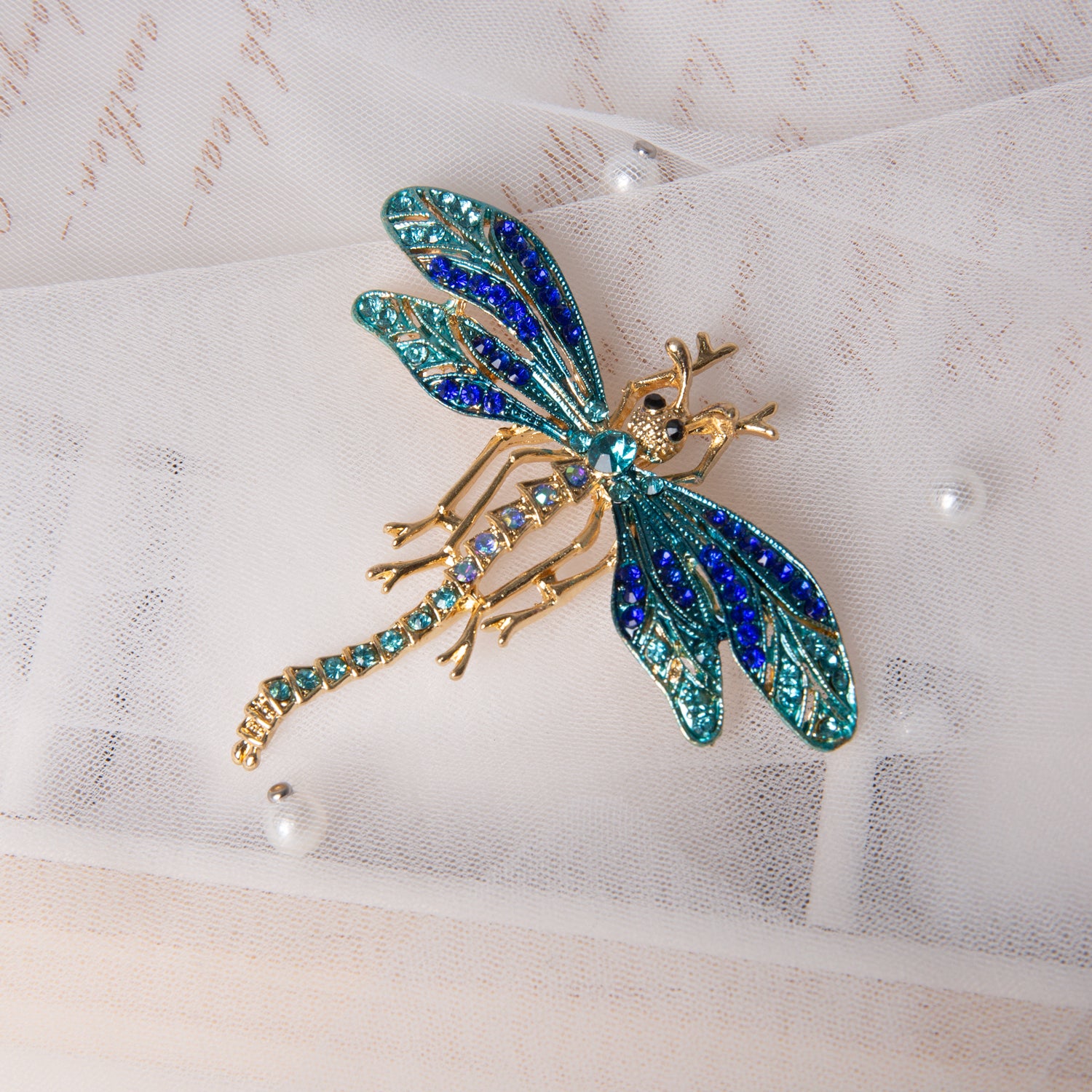 Enchanting Fairy Queen Brooch with blue and green gemstones on gold finish, displayed on white fabric with pearl beads at Lovful