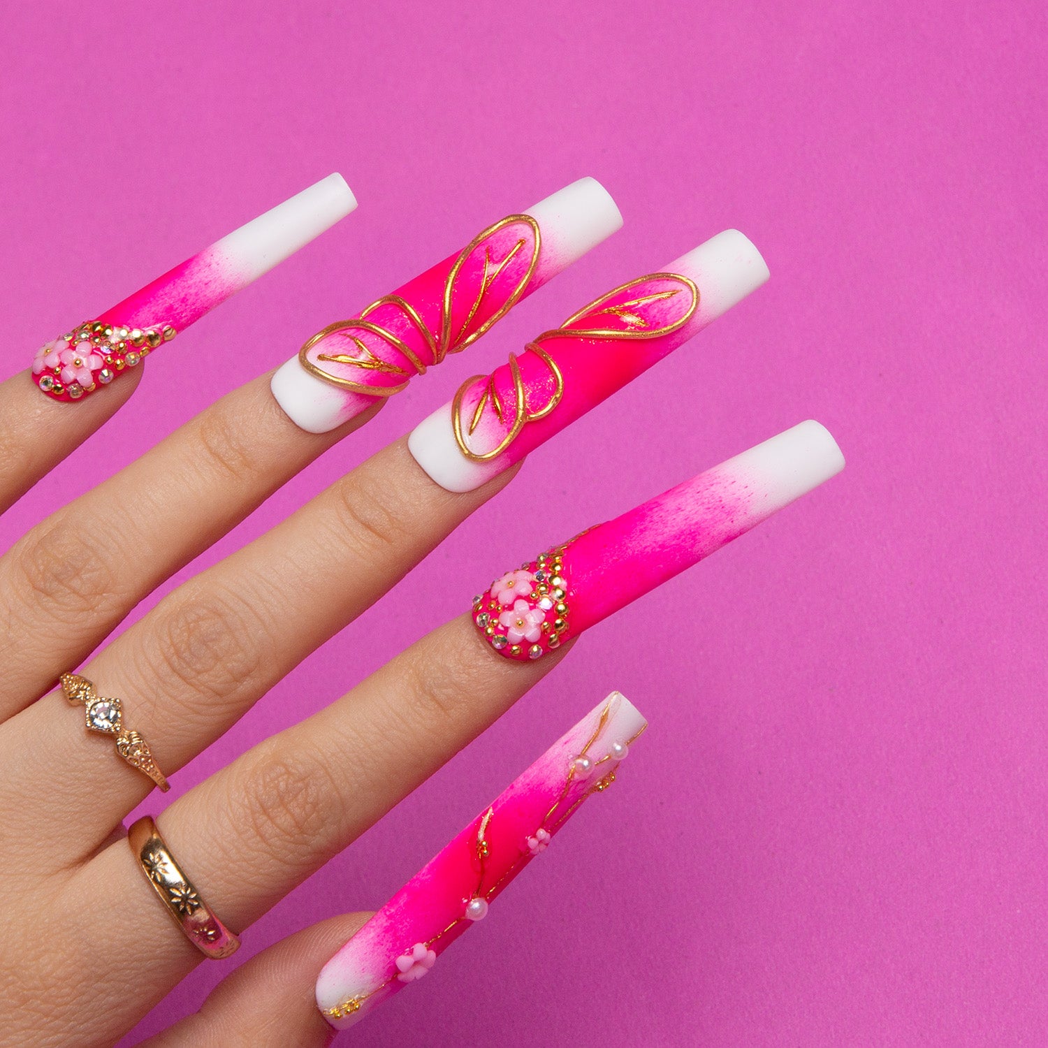 Hand showcasing Cherry Blossom square press-on nails with gradient pink and white base, 3D floral accents, and gold embellishments against a vibrant pink background.