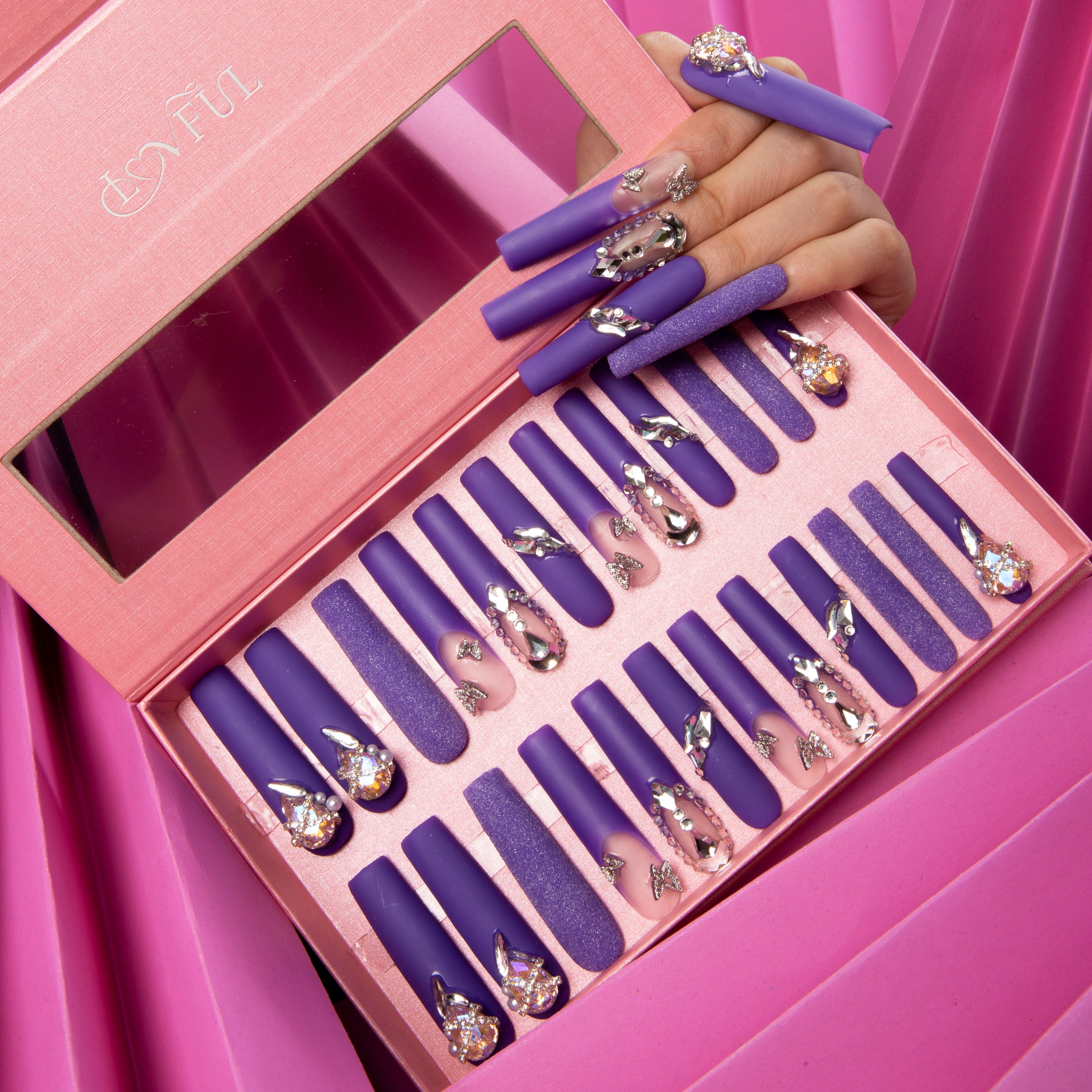 Set of 24 Mystique Veil press-on nails with deep purple base, butterfly decorations, gem accents, and glitter overlay in a pink box with Lovful logo.
