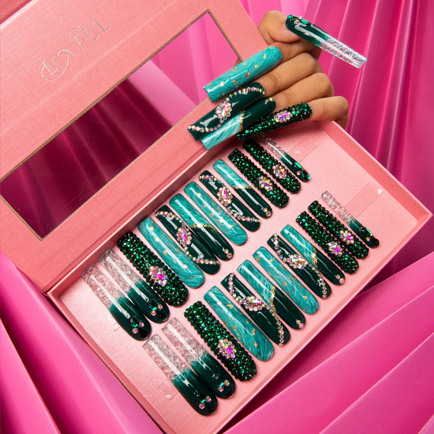 Emerald Envy press-on nails set in pink box, featuring intricate gold decor and green liquid design with rhinestones. Hand showing applied nails for Lovful.com product page.
