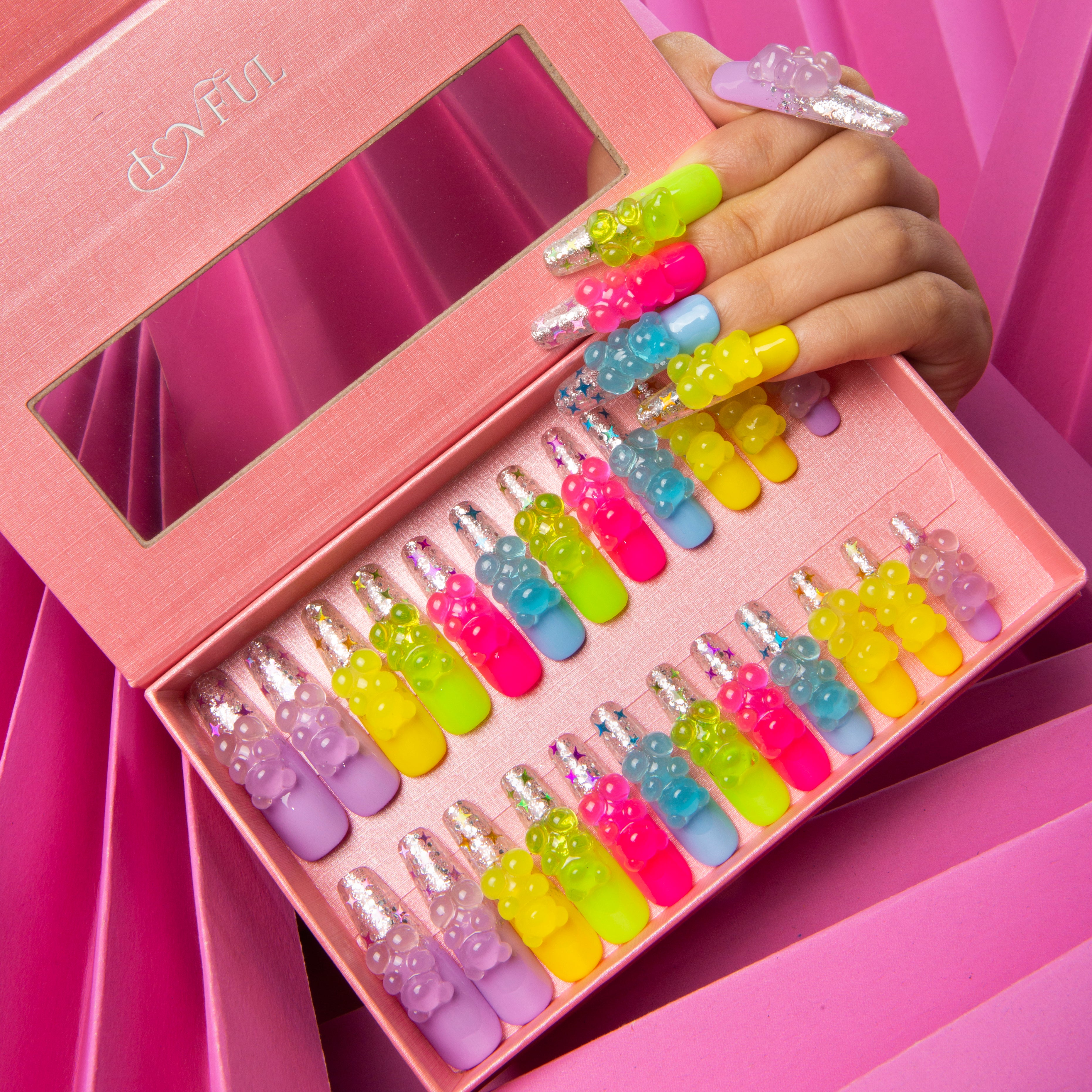 24-piece set of Lovful 'Sweet Wonderland' colorful press-on nails with glowing gummy bear charms. Nails are displayed in a pink box with a transparent window. Nail colors include candy pink, sunshine yellow, and more vibrant shades.
