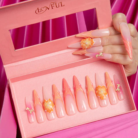 Lovful's nail art features elegant, pointed nails with a gradient of pink to orange and delicate flower decorations.