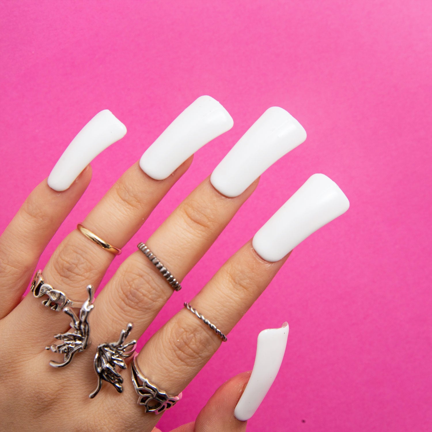 Hand wearing long white press-on acrylic nails in duck shape with silver rings against a pink background, showcasing Lovful's Snow White - Duck nails