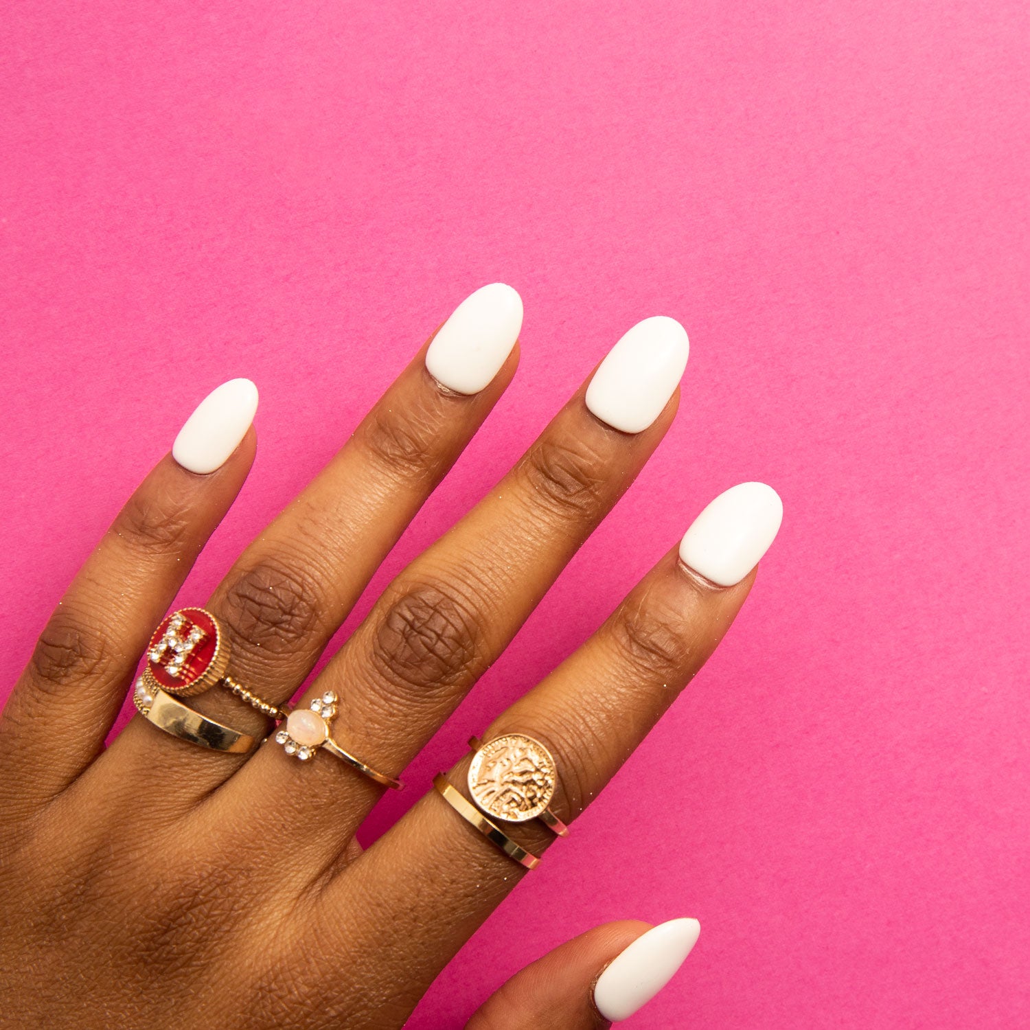 Hand with white round-shaped press-on acrylic nails wearing four gold rings against a bright pink background. Showcasing Lovful's H10 Snow White Round press-on nails.