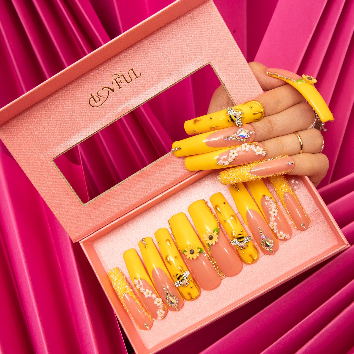 Lovful's H101 Honey Bee Curve press-on acrylic nails with bright yellow and pink designs, sunflower patterns, and bee accents, displayed in a pink box against a pink background.