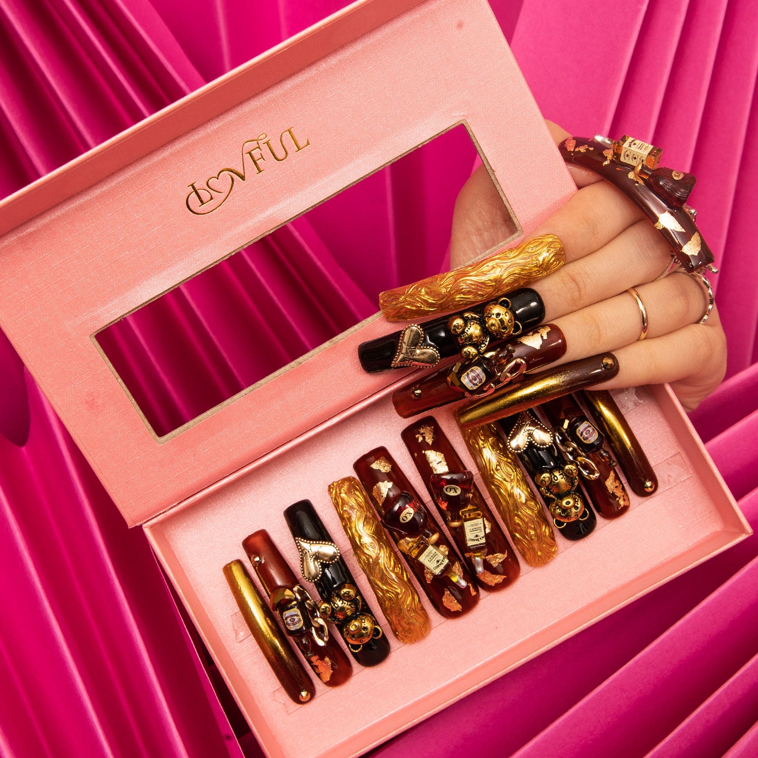 'Casino Party' press-on nails by Lovful, featuring black and gold design with bear and heart-shaped gems, and a wine bottle charm, displayed in an open pink box.