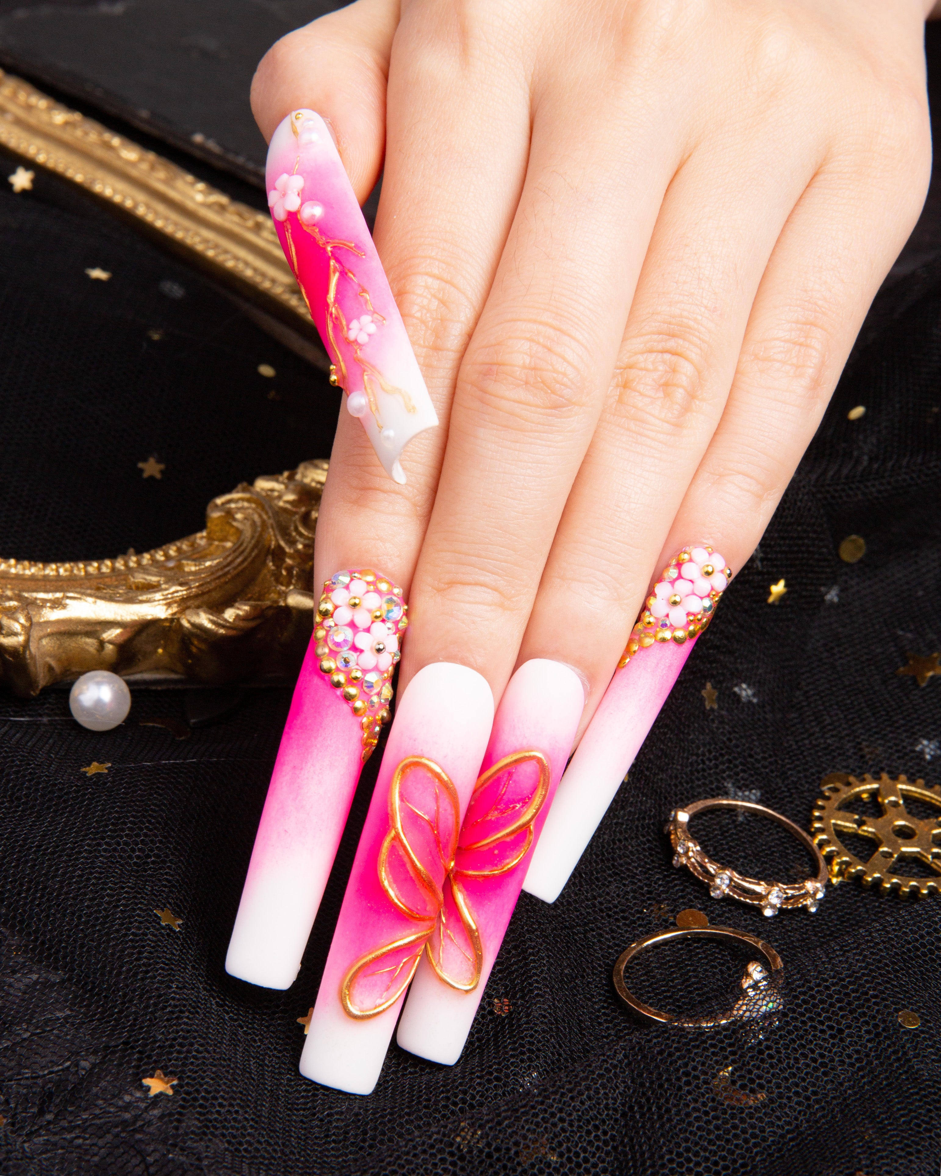 hand with long, gradient pink and white press-on nails featuring golden butterflies and beaded accents