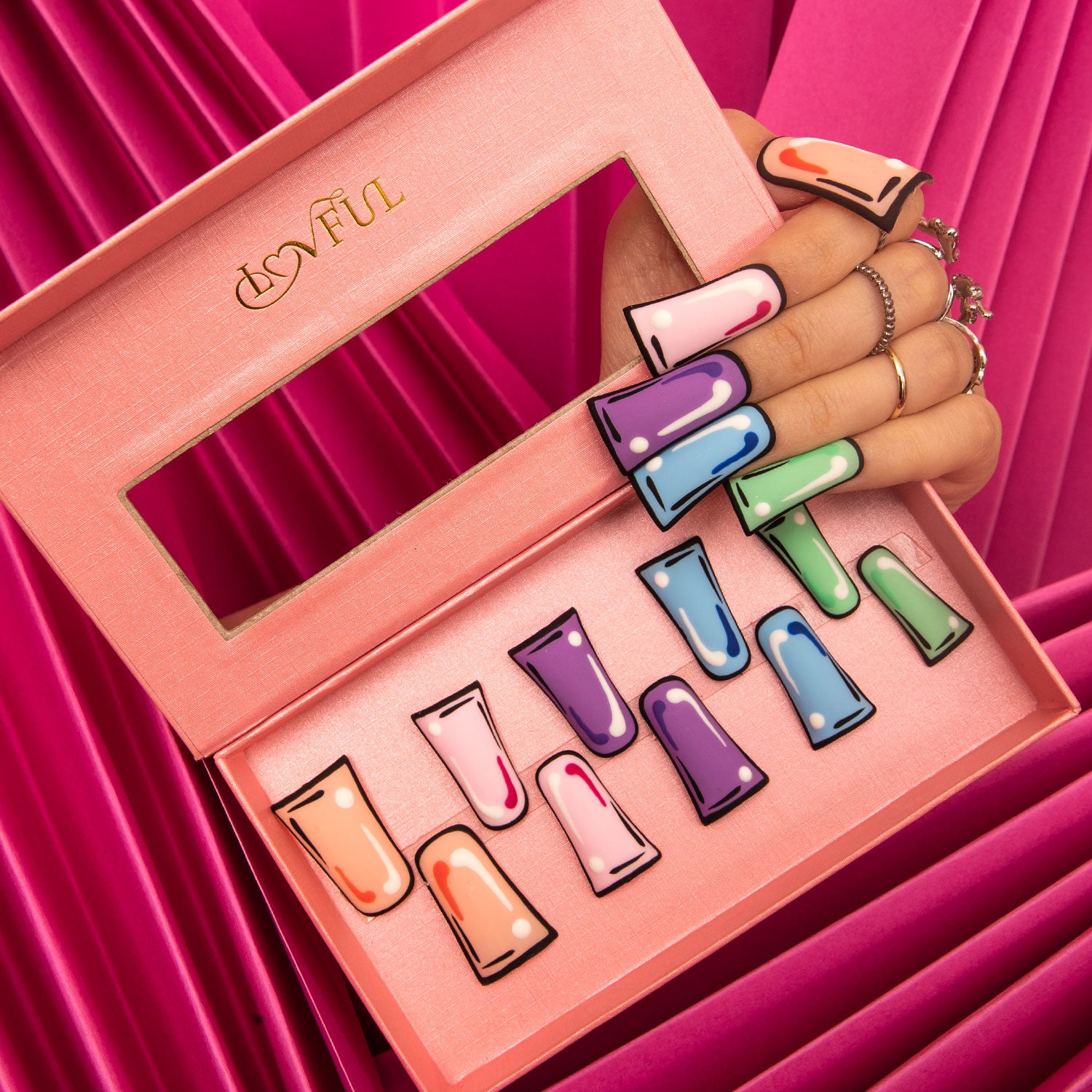 Lovful 'Colorful Pop' press-on nail set with vibrant pop art designs in a pink box. Includes various colors like orange, pink, purple, blue, and green. A hand with matching nails holds the lid of the box.