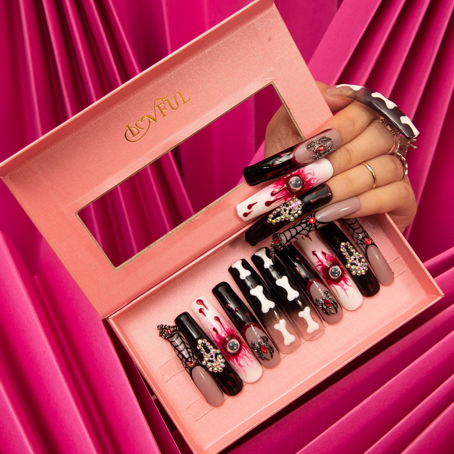 Final Destination press-on nails in a Lovful pink box. The Halloween-themed designs include ghost faces, skeletal bones, sinister eyes, and blood-red hues, with a hand showcasing matching nails against a pink backdrop.