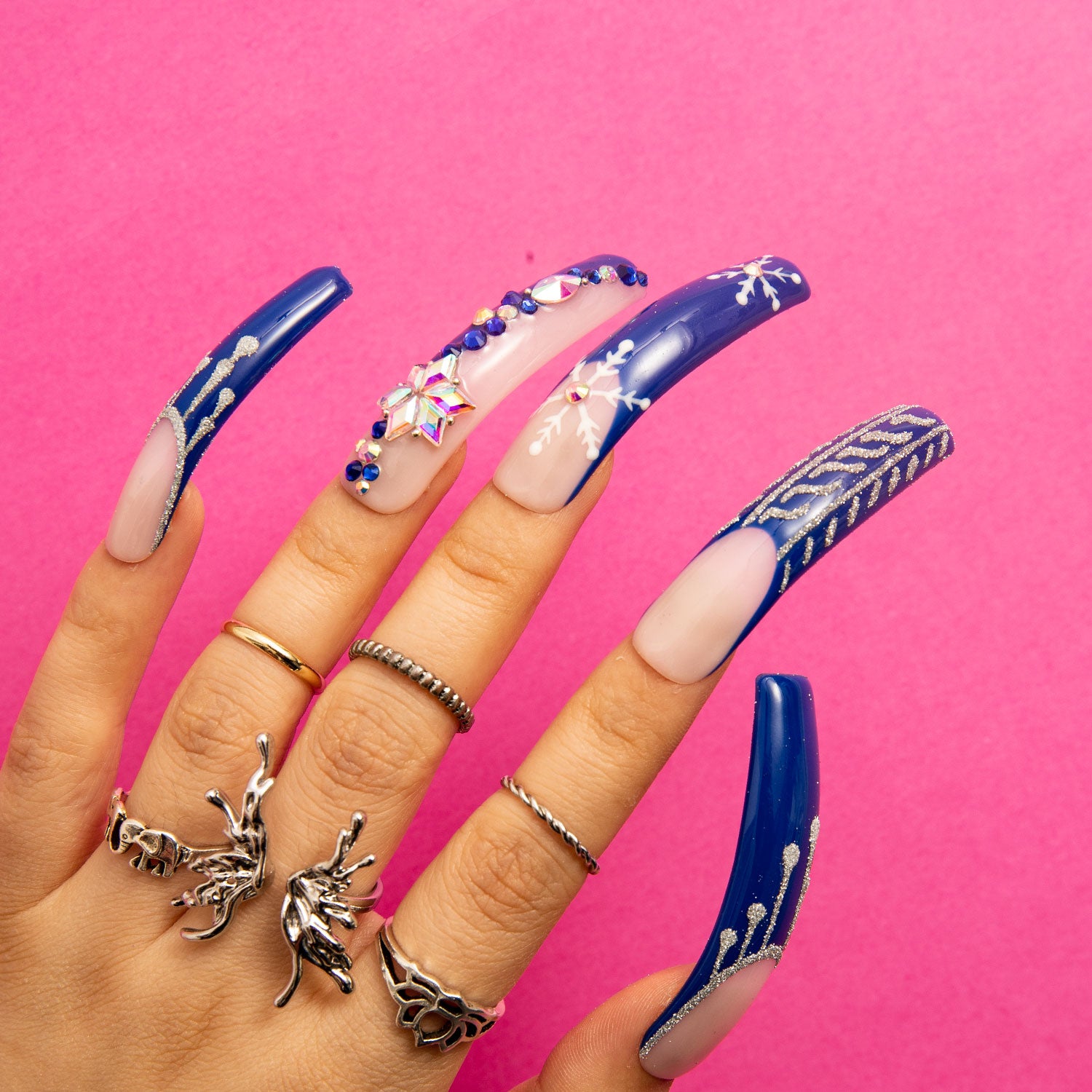 Hand with long blue French tip press-on nails featuring delicate white snowflake designs, jewelry-inspired decorations, and intricate patterns, from Lovful's Snow Waltz collection.
