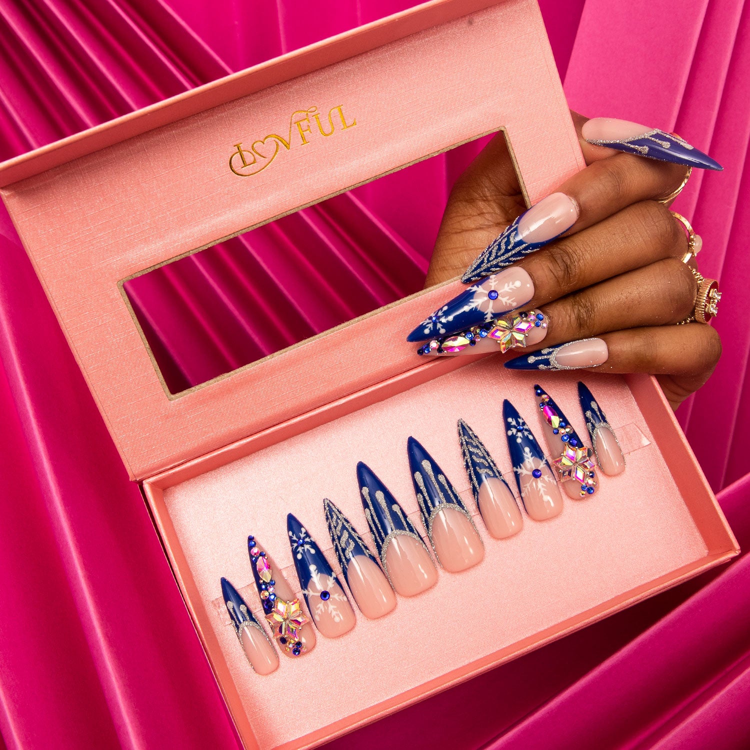 Lovful Snow Waltz press-on nails with blue French tips and white snowflakes, displayed in a pink box, against a vibrant pink background.