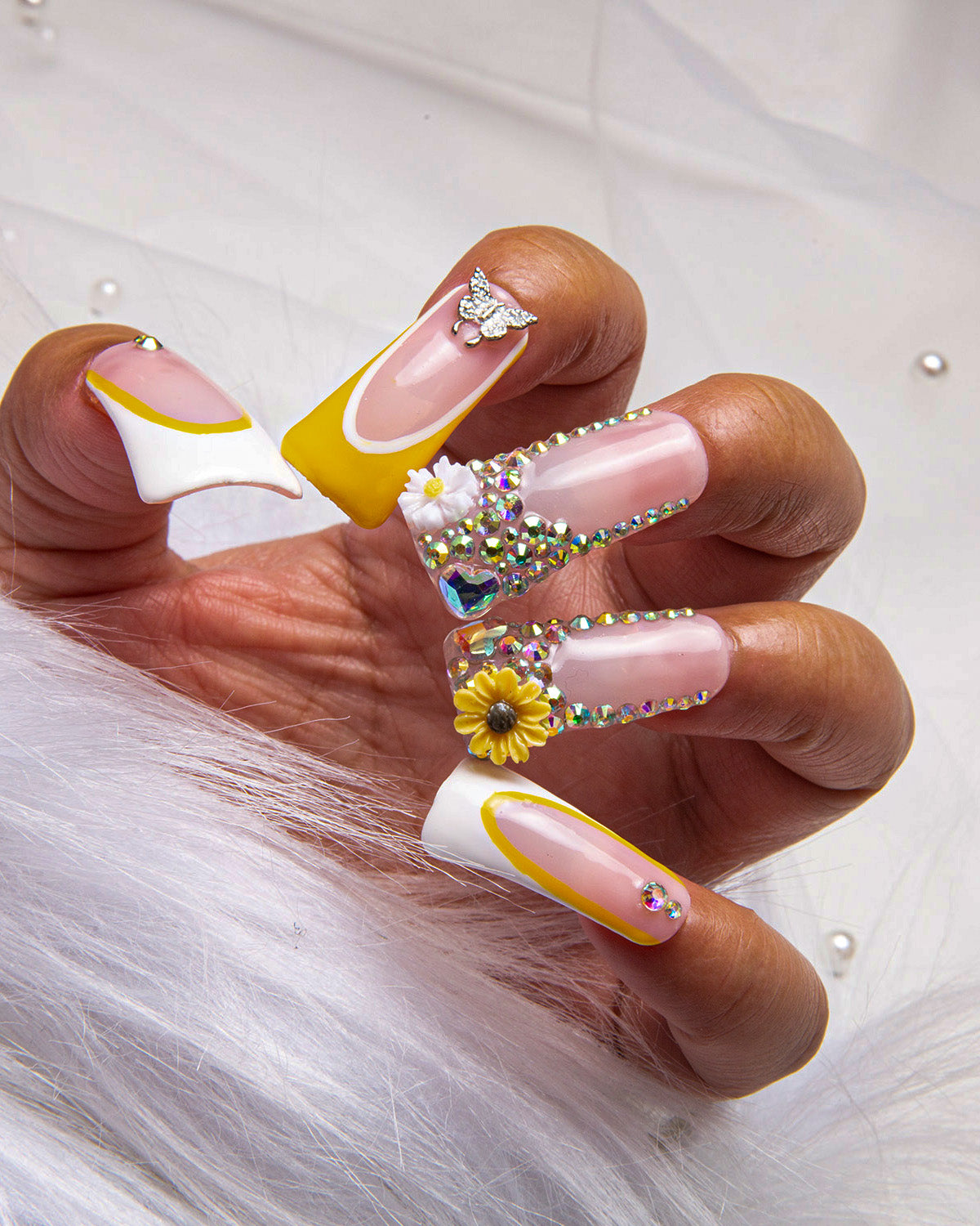 Hand displaying 'Sunflower' 24-piece press-on nail set from Lovful.com, featuring white and yellow French tips, rhinestones, a sunflower design, and a butterfly ornament.