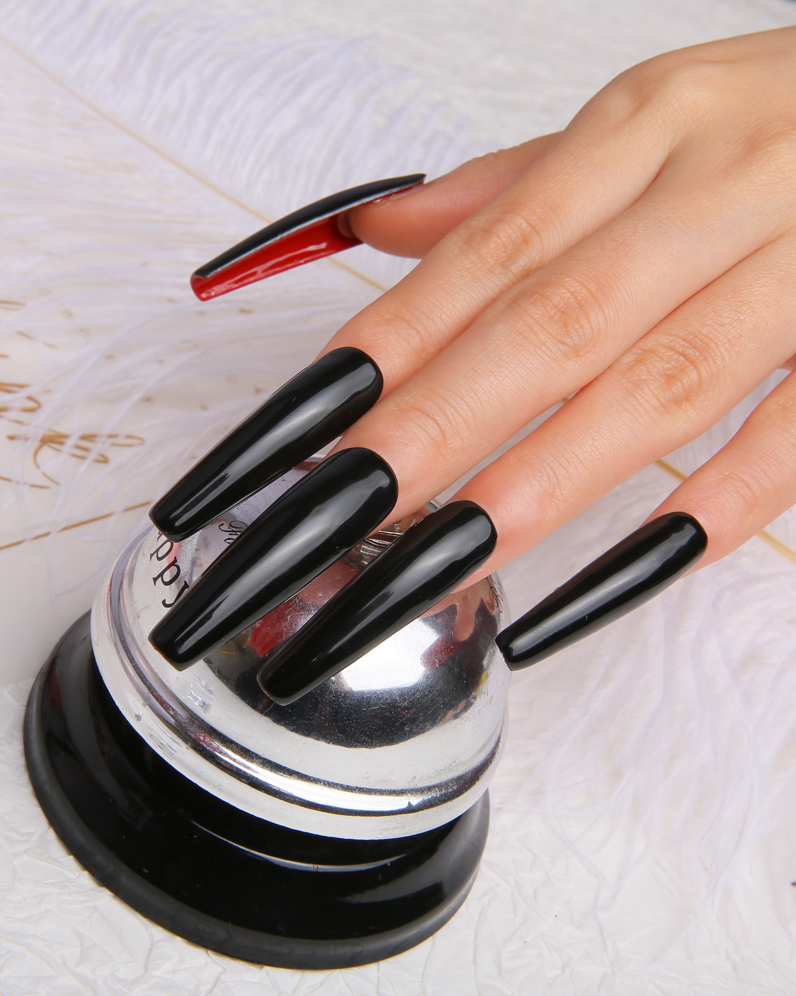 Hand wearing press-on nails with sleek black finish and striking red underside, displayed on a silver prop. Coffin-shaped design for chic and bold look.