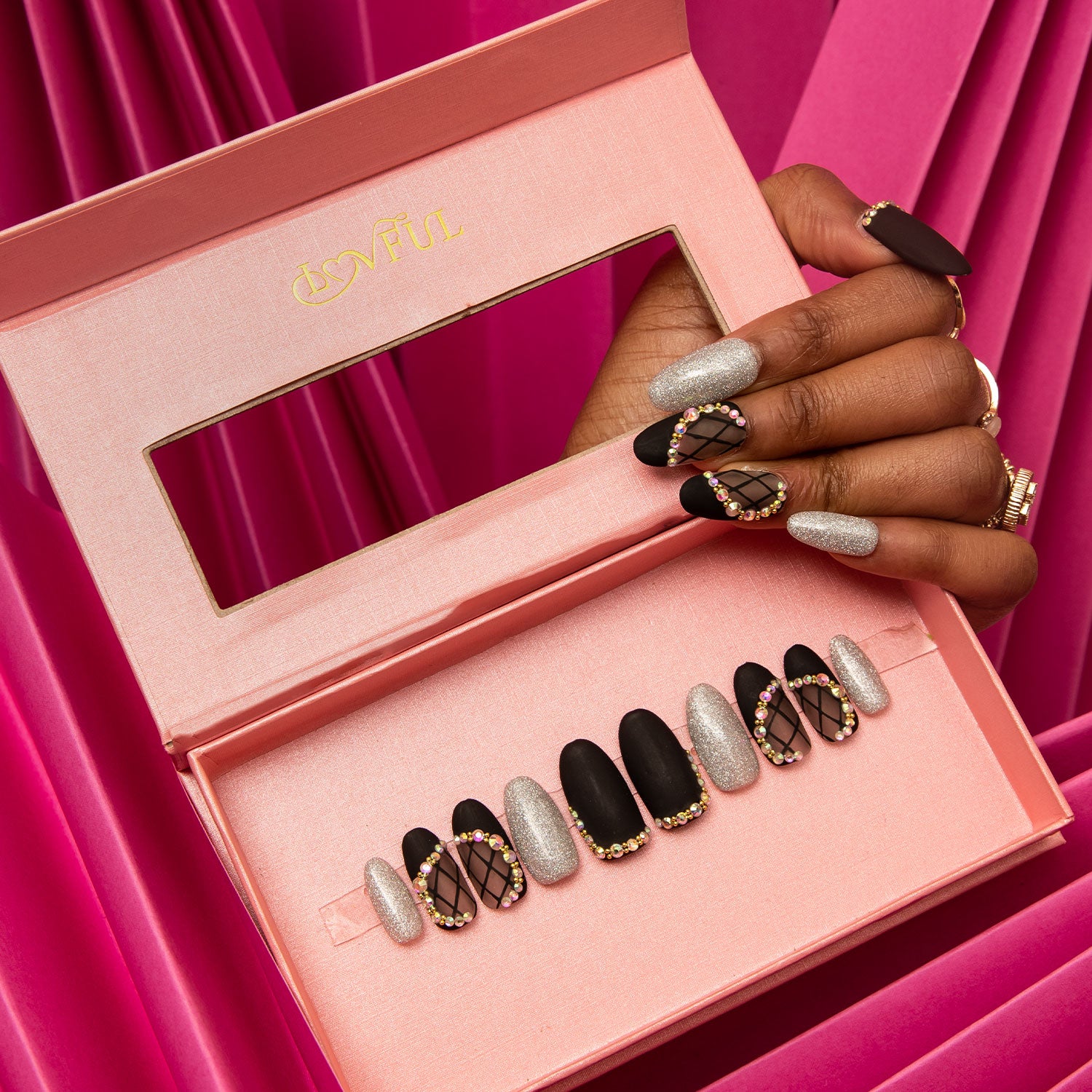 Black Lace press-on nails set from Lovful in an open pink box with distinct black and silver designs, including lace and rhinestone accents, placed against a vibrant pink background.