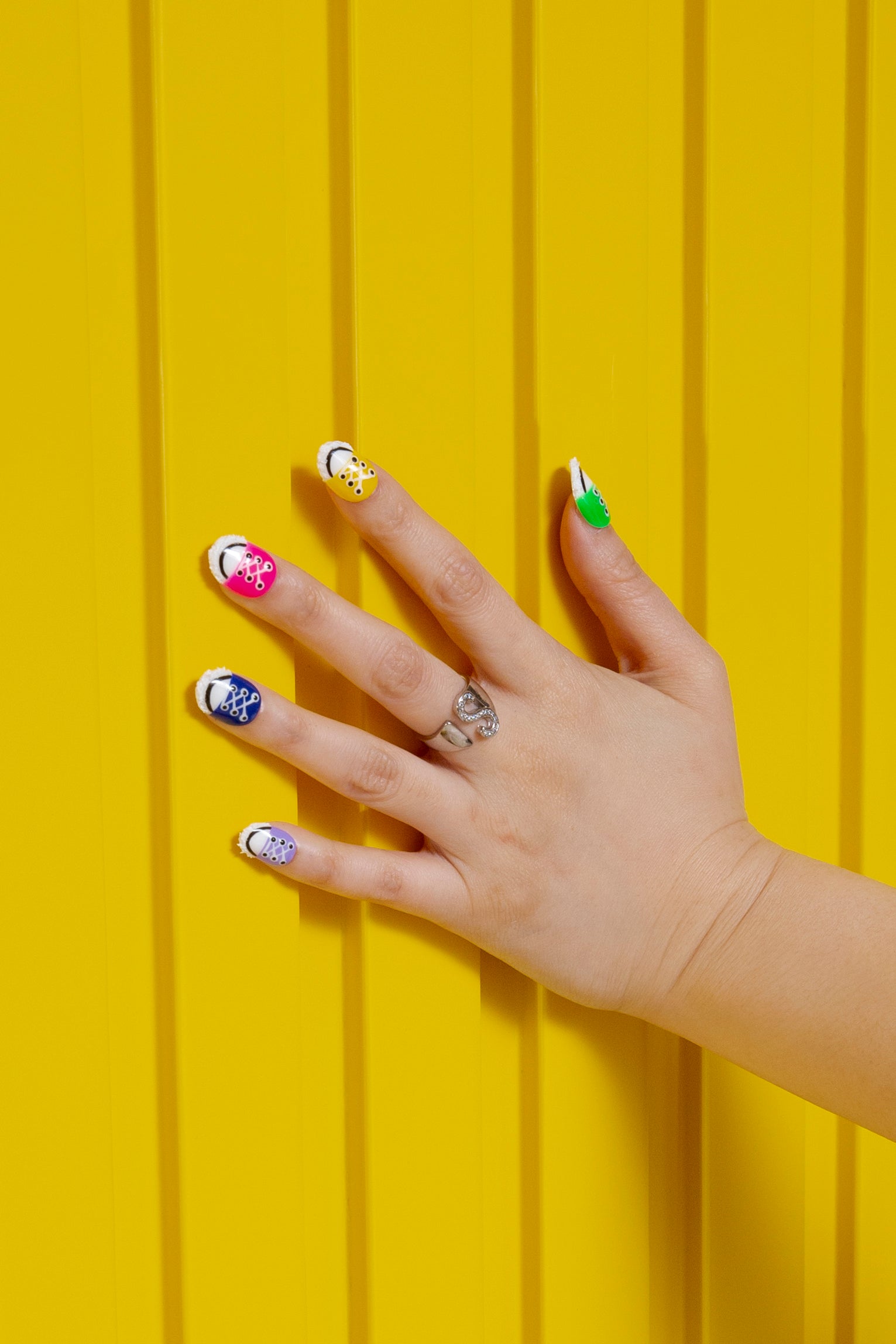 Hand displaying colorful press-on nails with floral and geometric designs against a vibrant yellow background, showcasing Lovful's 'H100 - Walk in Spring - 24 pcs' collection.