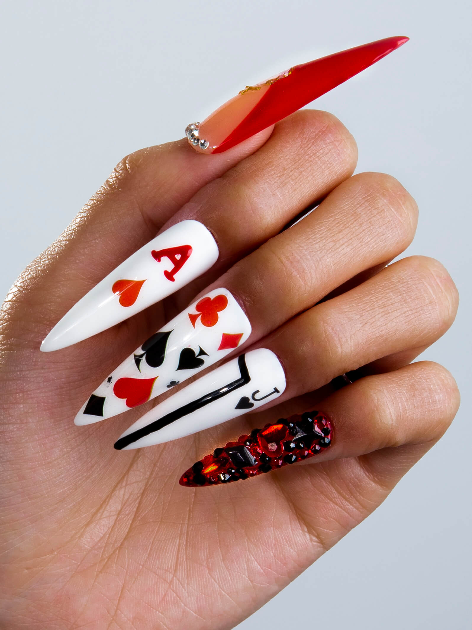 Close-up of press-on stiletto nails with poker card designs, including hearts, spades, diamonds, and clubs. Features red ace and Queen of Hearts designs from Poker Queen collection at Lovful.com