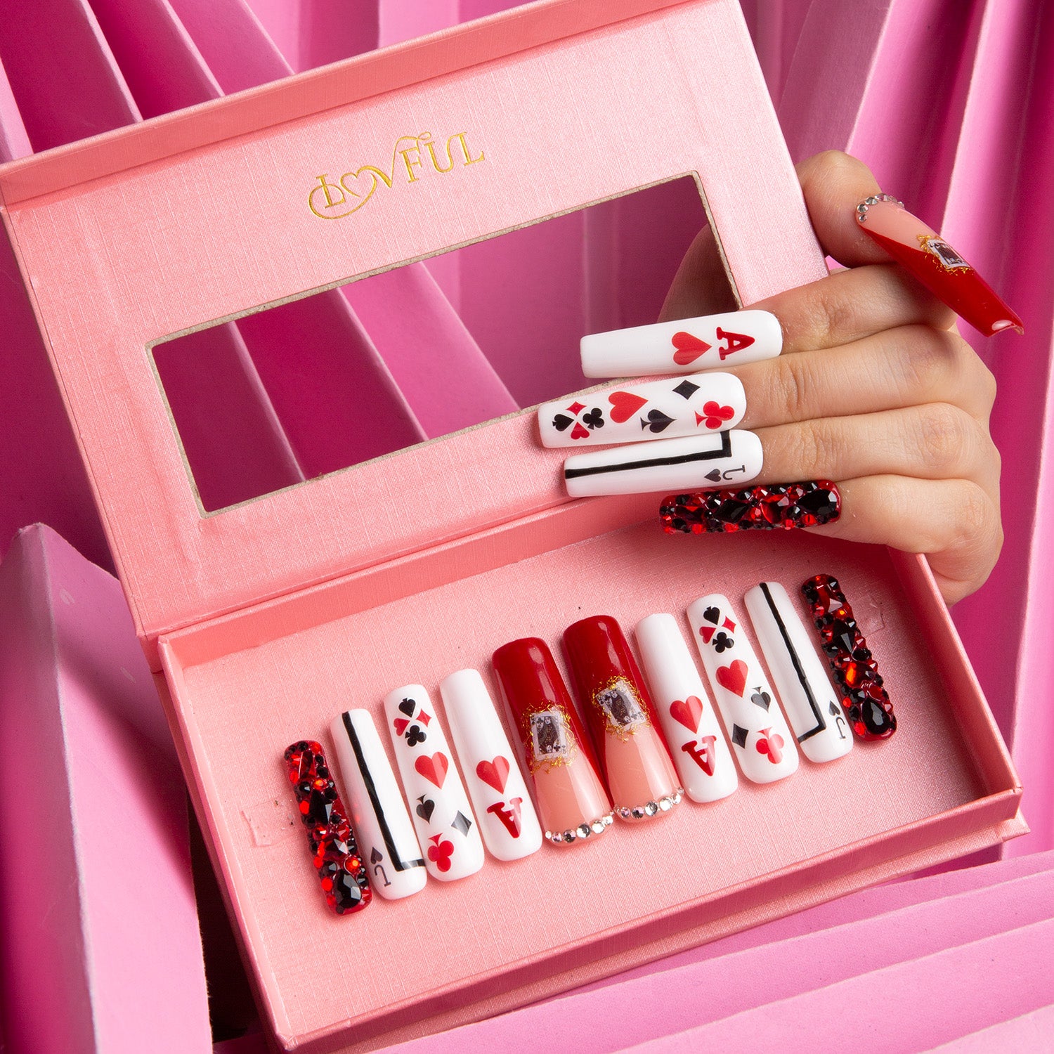 Poker Queen press-on nail set displayed in a pink box with various red and white card-themed designs, including hearts, spades, and a Queen of Hearts motif. Hand showcasing the nails.