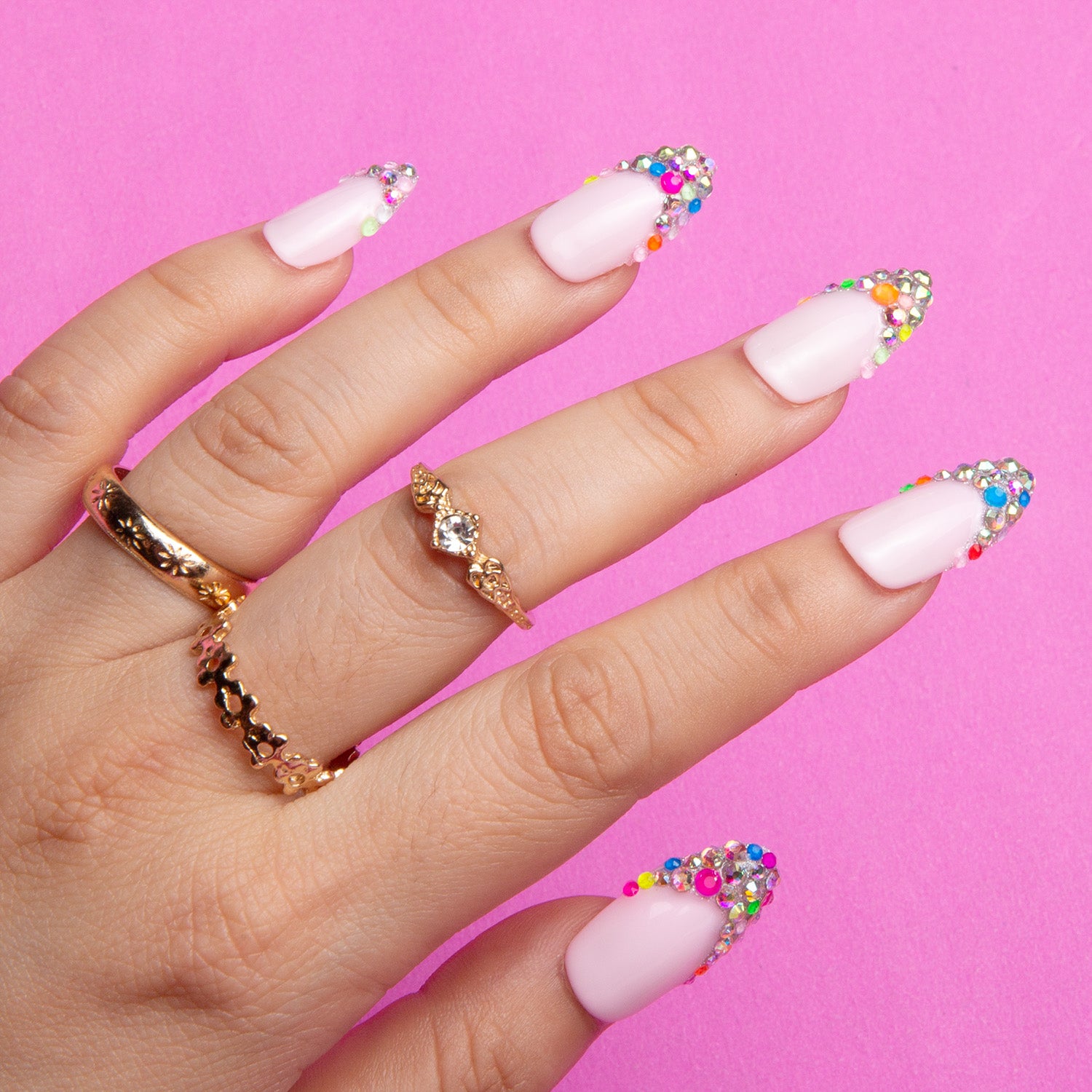 Press-on nails with Jelly Bean design, nude base with colorful beads on tips, worn by hand with gold rings, against a pink background. Part of Lovful's 'H125 - Jelly Beans - Almond' collection.