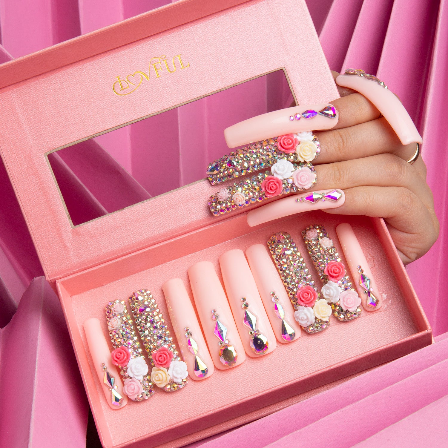 Lovful Rose Garden Bliss press-on nails in pink box. Nails are adorned with roses and rhinestones, arranged on a hand and in the box, showcasing their romantic and detailed design.