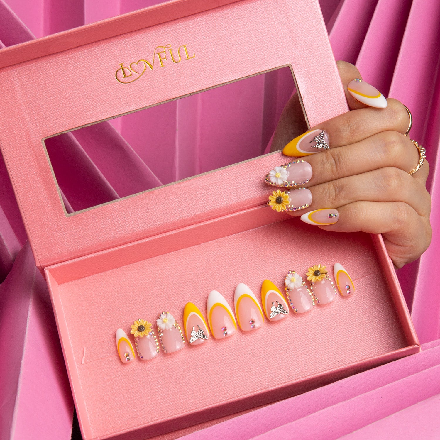 Almond-shaped 'Sunflower' press-on nails by Lovful with vibrant yellow and white French tips, sunflower designs, and sparkling embellishments in a pink box.