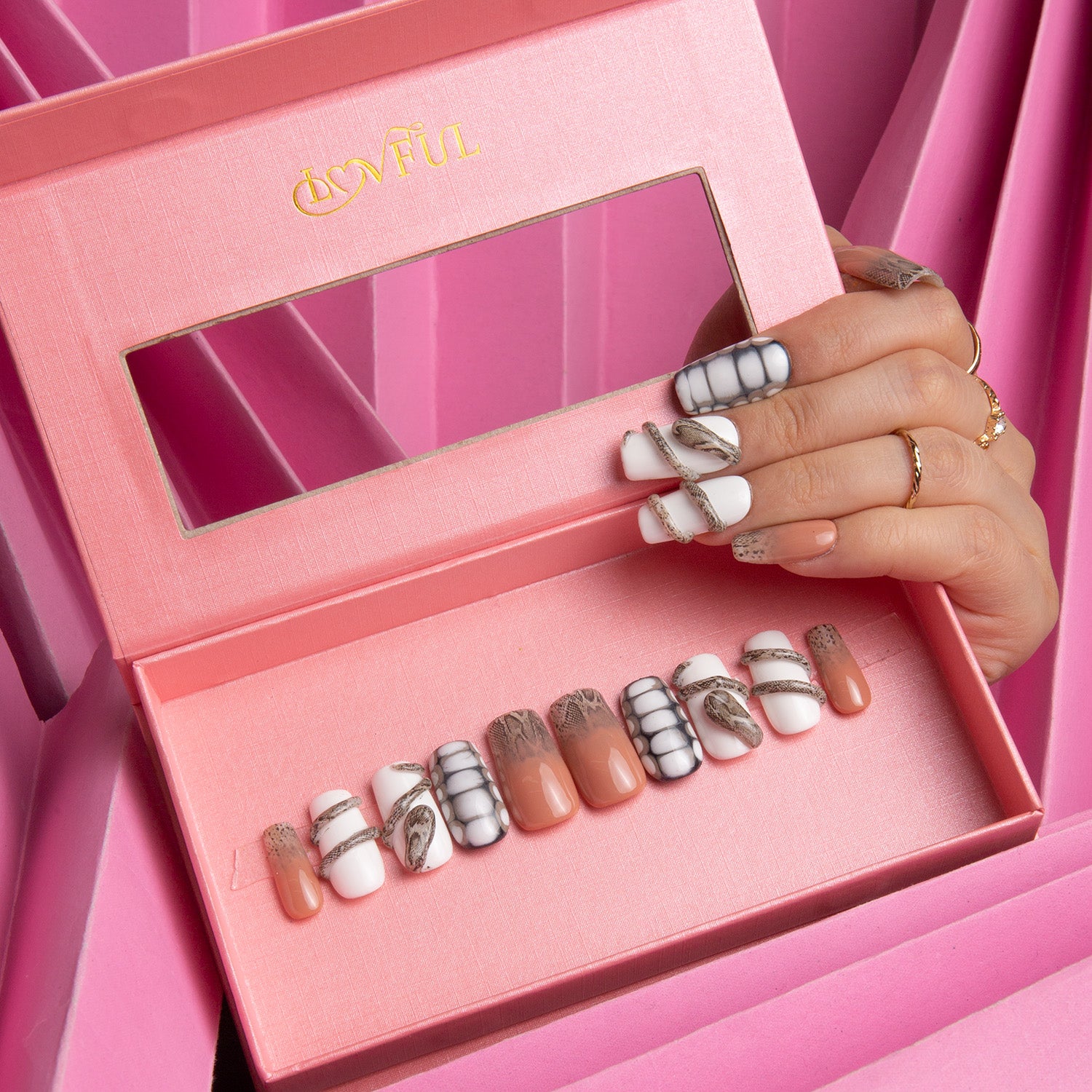 Lovful 'Sahara' press-on nail set in a pink box, featuring pure white base with subtle sand effect, snake designs, and various patterns. A hand with similar manicured nails is holding the box.
