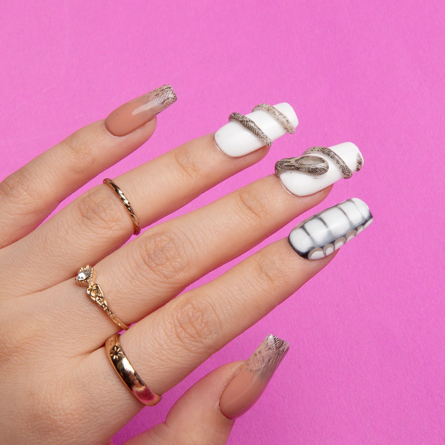 'Sahara' press-on nail set by Lovful.com showcasing white base nails with a subtle sand effect and snake design, displayed on a hand with gold rings against a pink background.