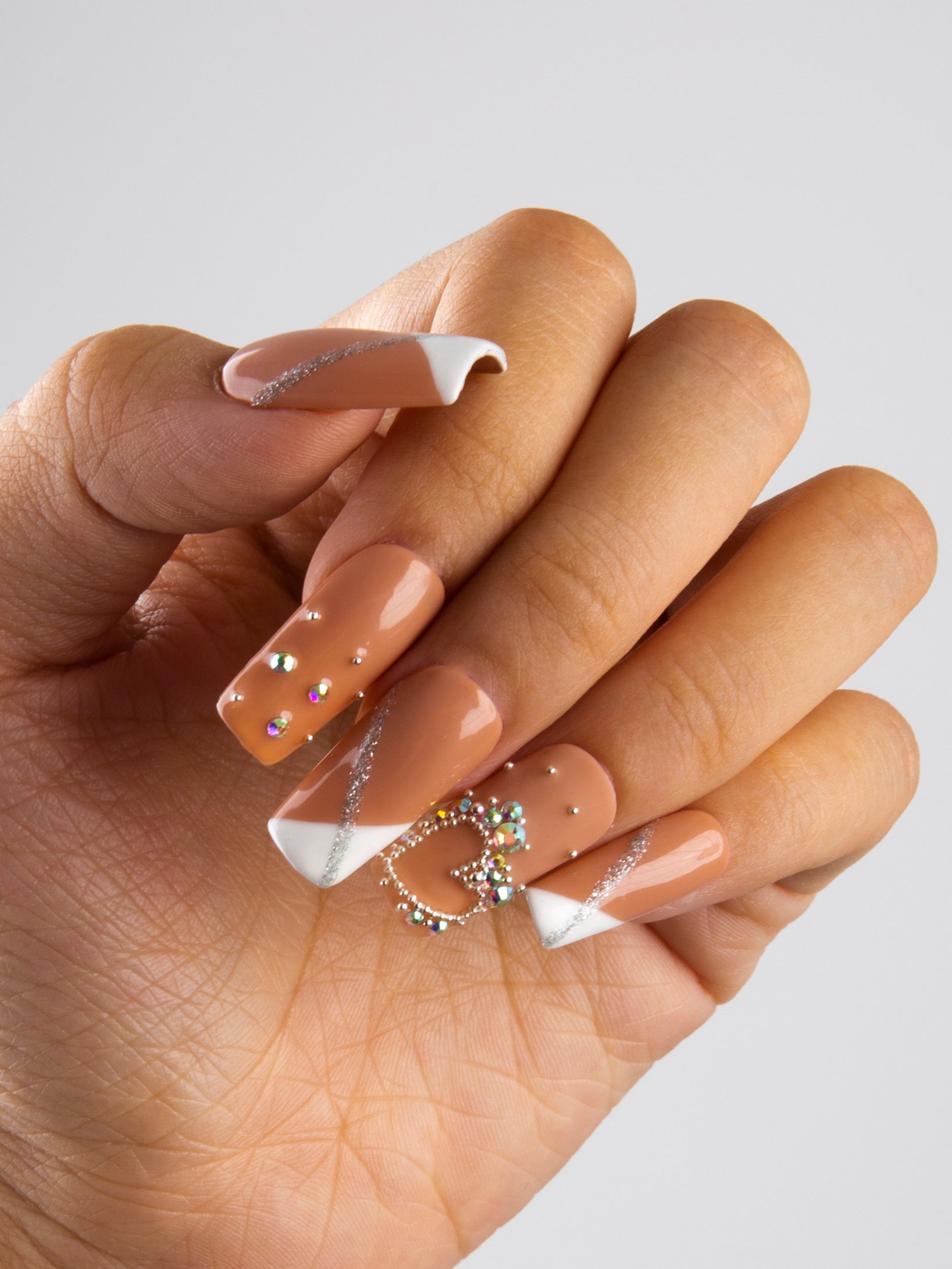 Hand with 'Lovely Kitten Heels' press-on nails set, featuring nude base, white French tips, silver glitter accents, and rhinestone bow on the middle nail.