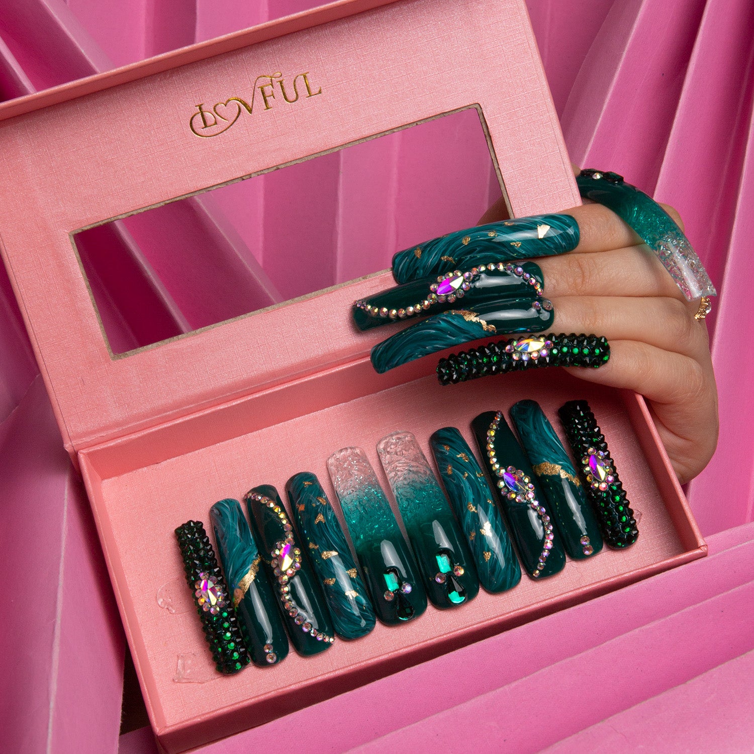 Emerald Envy Press-On Nails - Curve in an open pink Lovful box with a hand showing the nails. Green liquid flowing design with intricate gold and jeweled decor, resembling forest foliage.