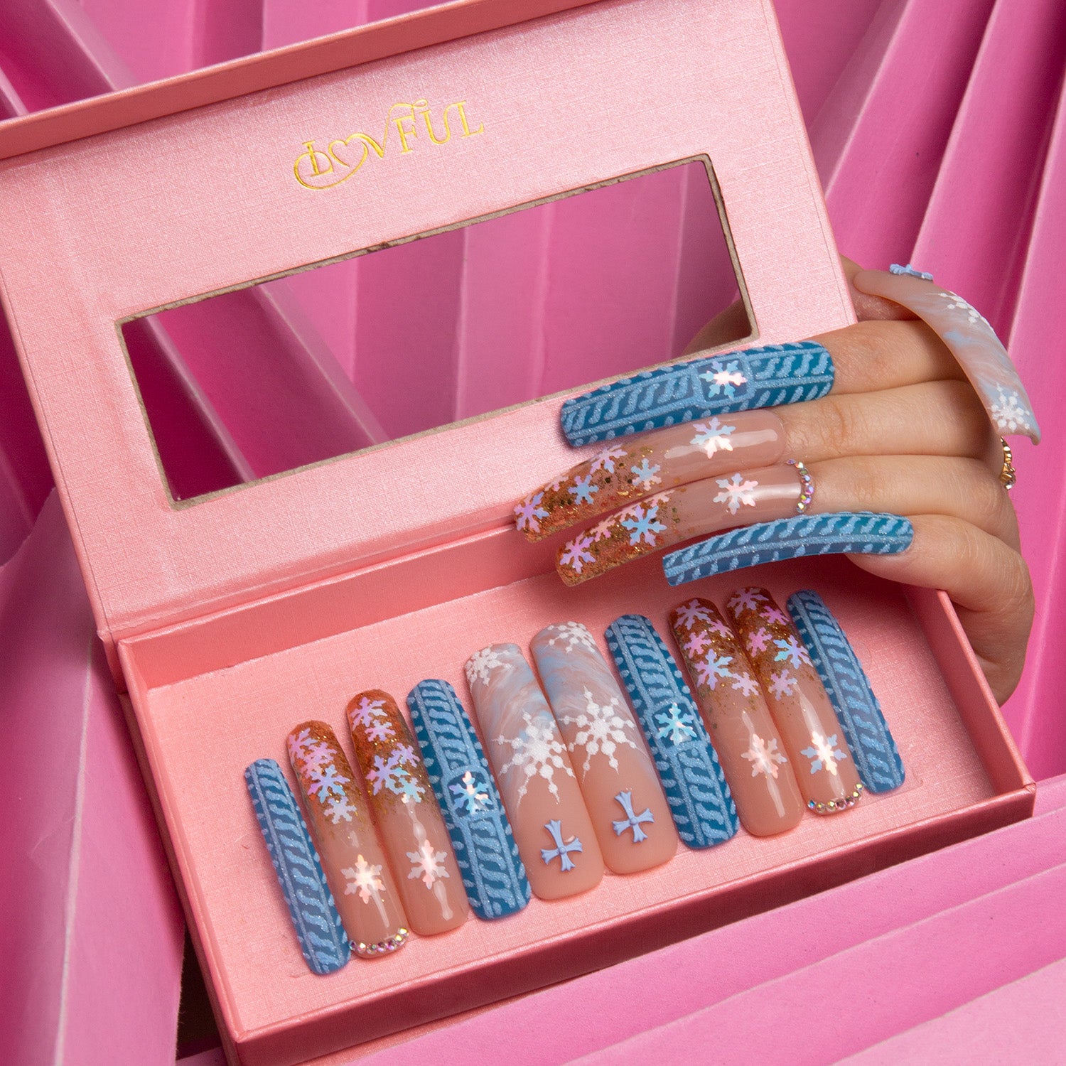 Set of 'Winter Sunshine' press-on nails by Lovful, displayed in a pink box. Nails have a gentle blue hue with gold glitter and white snowflake designs, capturing festive winter themes.