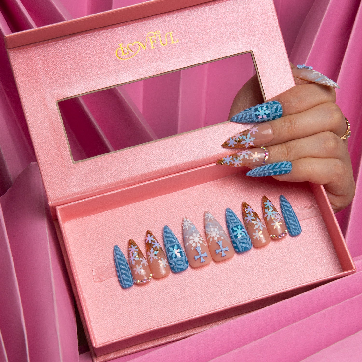 Lovful Winter Sunshine stiletto press-on nails in a pink box, featuring soft blue hues, golden glitter, and snowflake designs. A hand showcases matching nails.