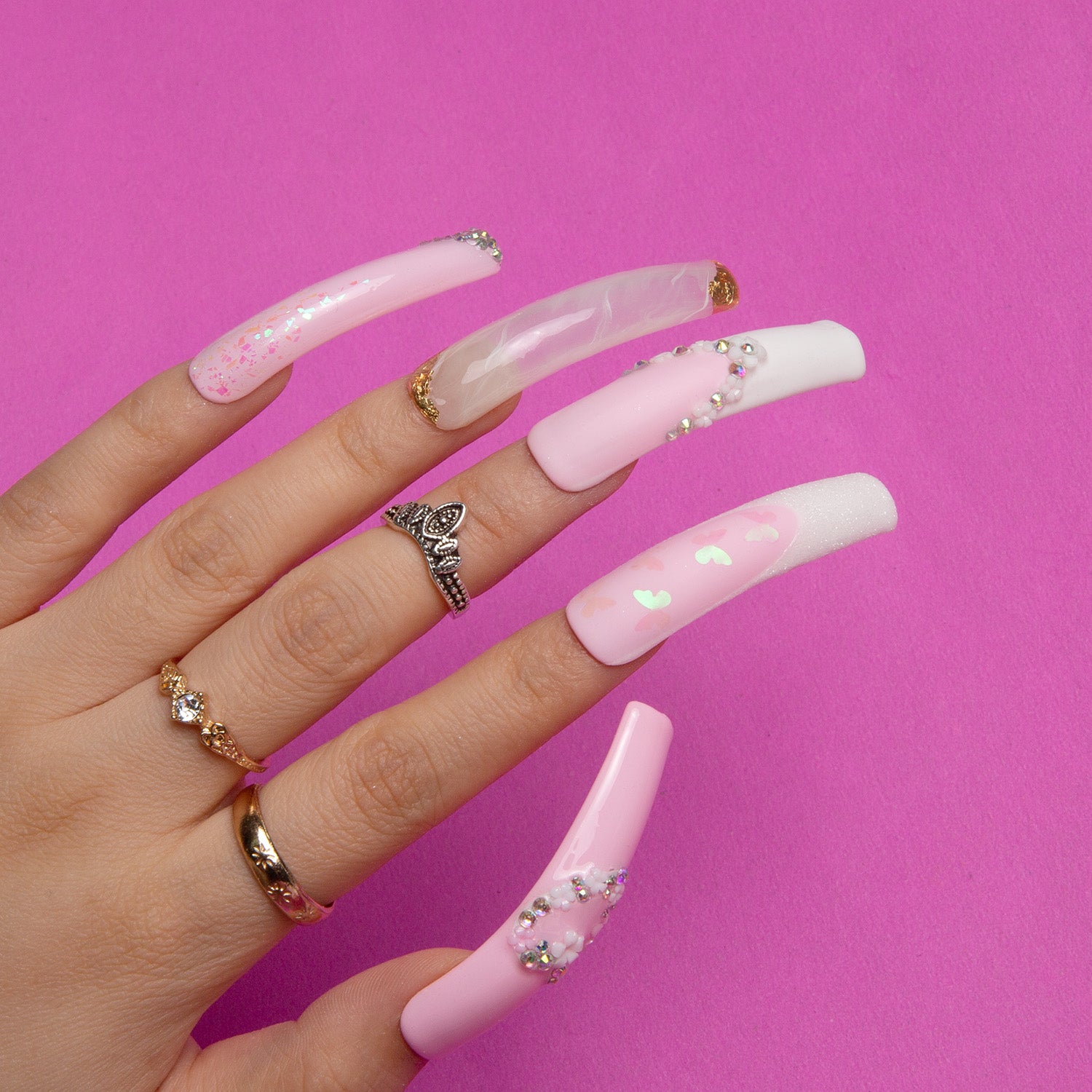 Hand wearing long, curved, pink and white press-on acrylic nails with French tips, heart-shaped flower designs, and bejeweled accents, ideal for bridal wear.