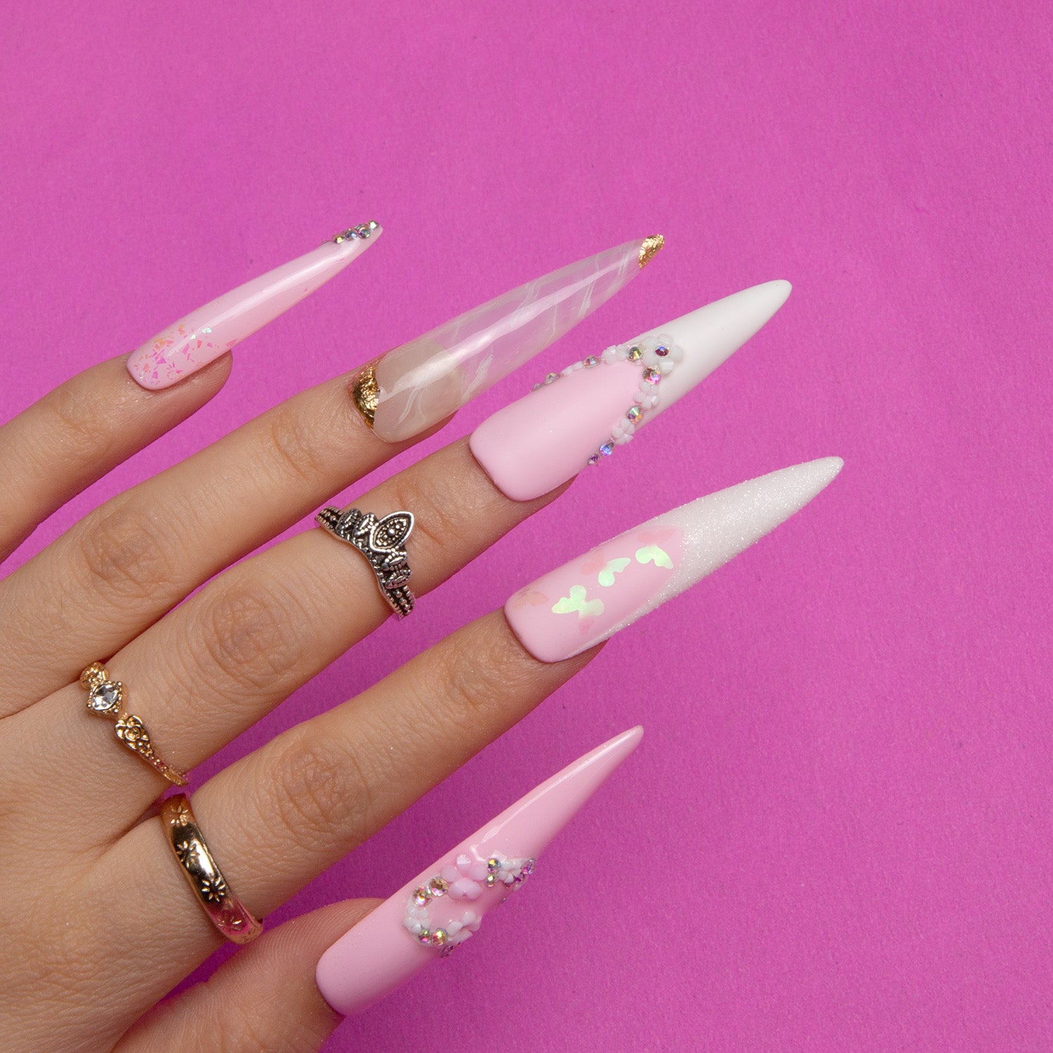 Stiletto-shaped press-on nails in light pink with heart-shaped flowers, French tips, beads, and glitter, ideal for bridal wear, against a pink background.