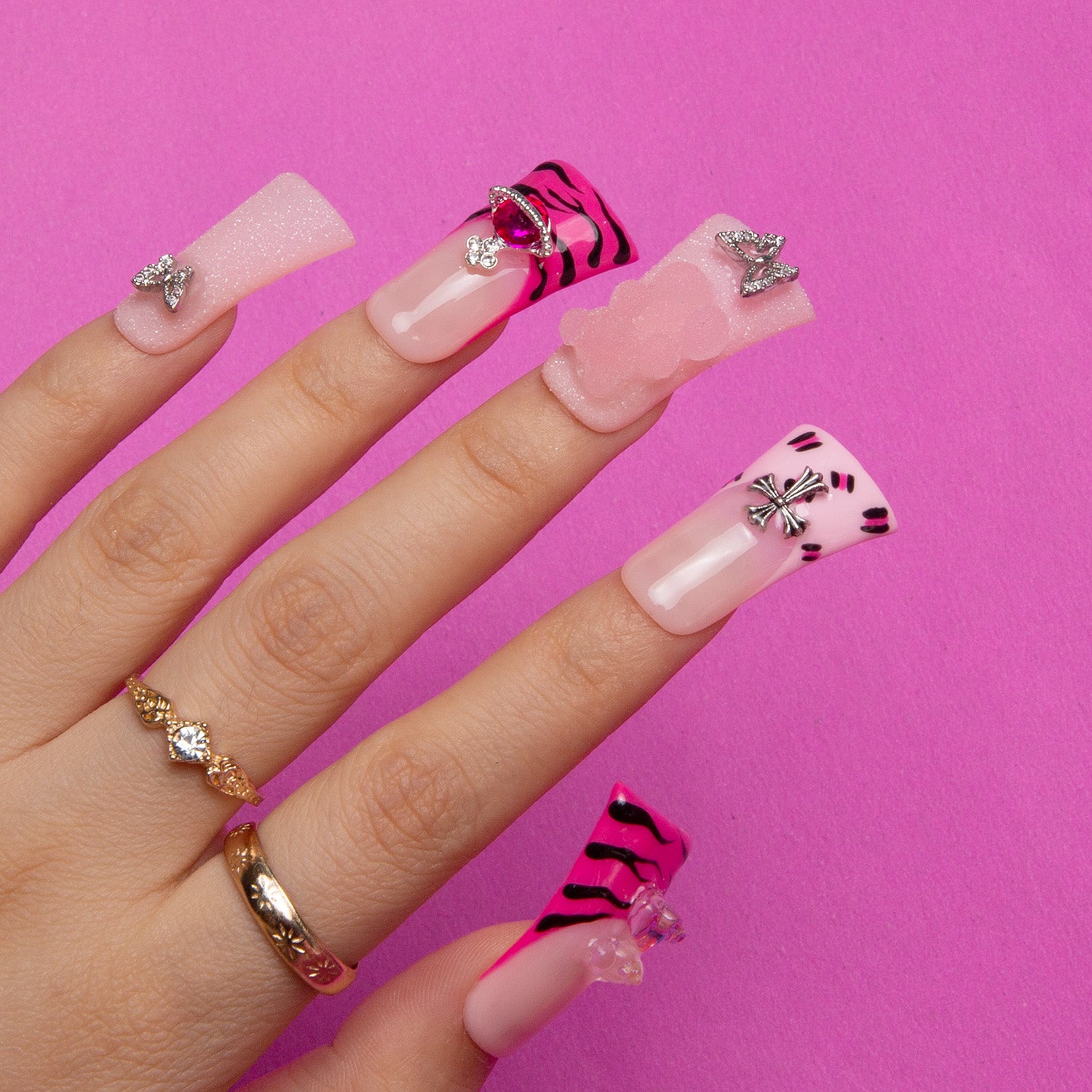 Hand showcasing Safari Love press-on acrylic nails with hot pink French tips, leopard prints, and decorative accents like lips and butterflies on a pink background.