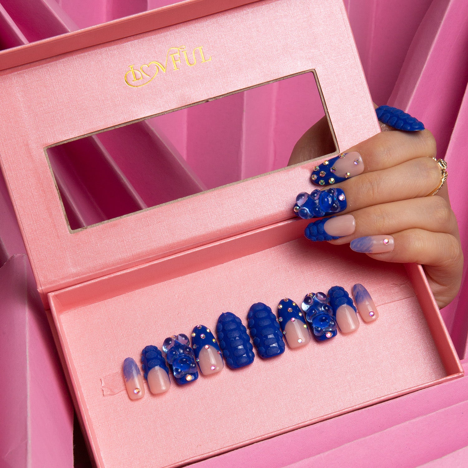 Little Blue Bear Rhinestone French tip press-on acrylic nails in a pink presentation box, featuring blue gummy bear designs and shiny rhinestones. Hand showcasing the nail design while holding the box.