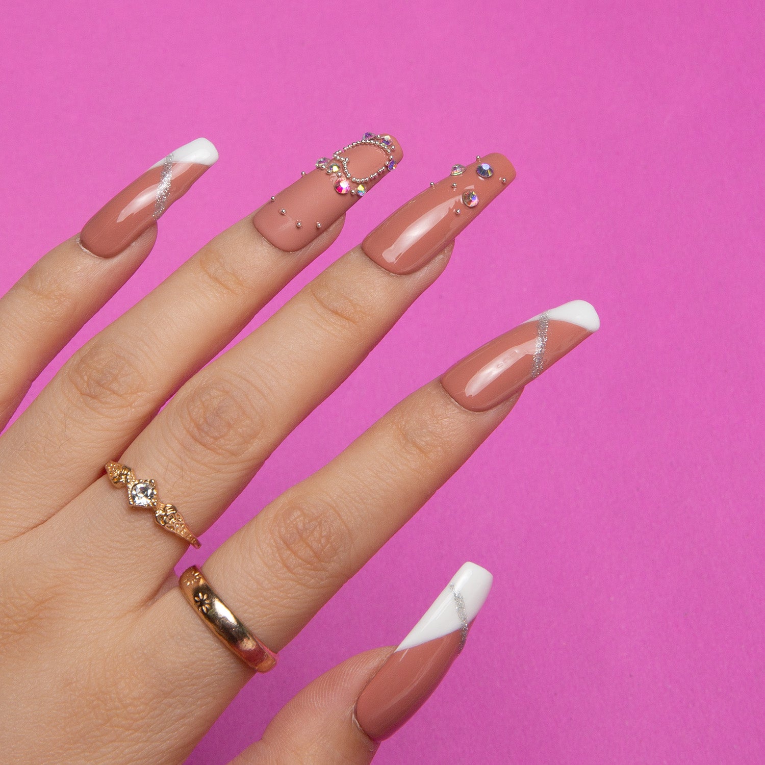 Press-on coffin-shaped nails with French tips, silver glitter, and rhinestone decorations from Lovful's 'Lovely Kitten Heels' collection. Hand wearing gold rings against a pink background.