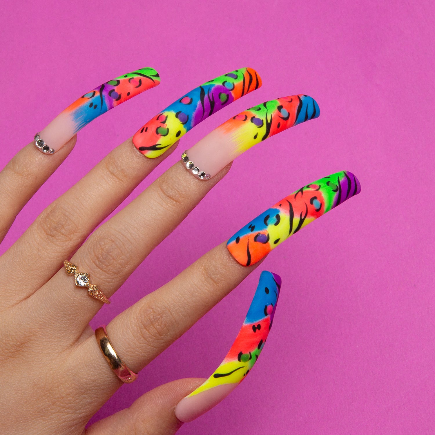 Hand with long, colorful French tip press-on nails featuring leopard print designs on bright gradient colors. Rings adorn the fingers, set against a vibrant pink background. Perfect for a bold and trendy look.