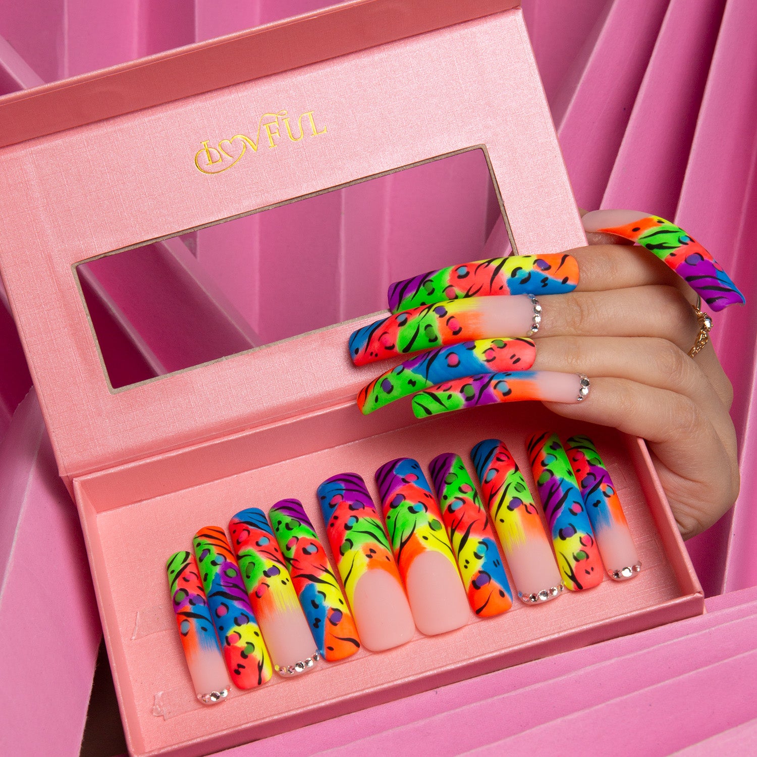 Hand showcasing press-on nails with bright colorful French tips and leopard prints. The nails are packaged in a pink box with Lovful logo, against a textured pink background.