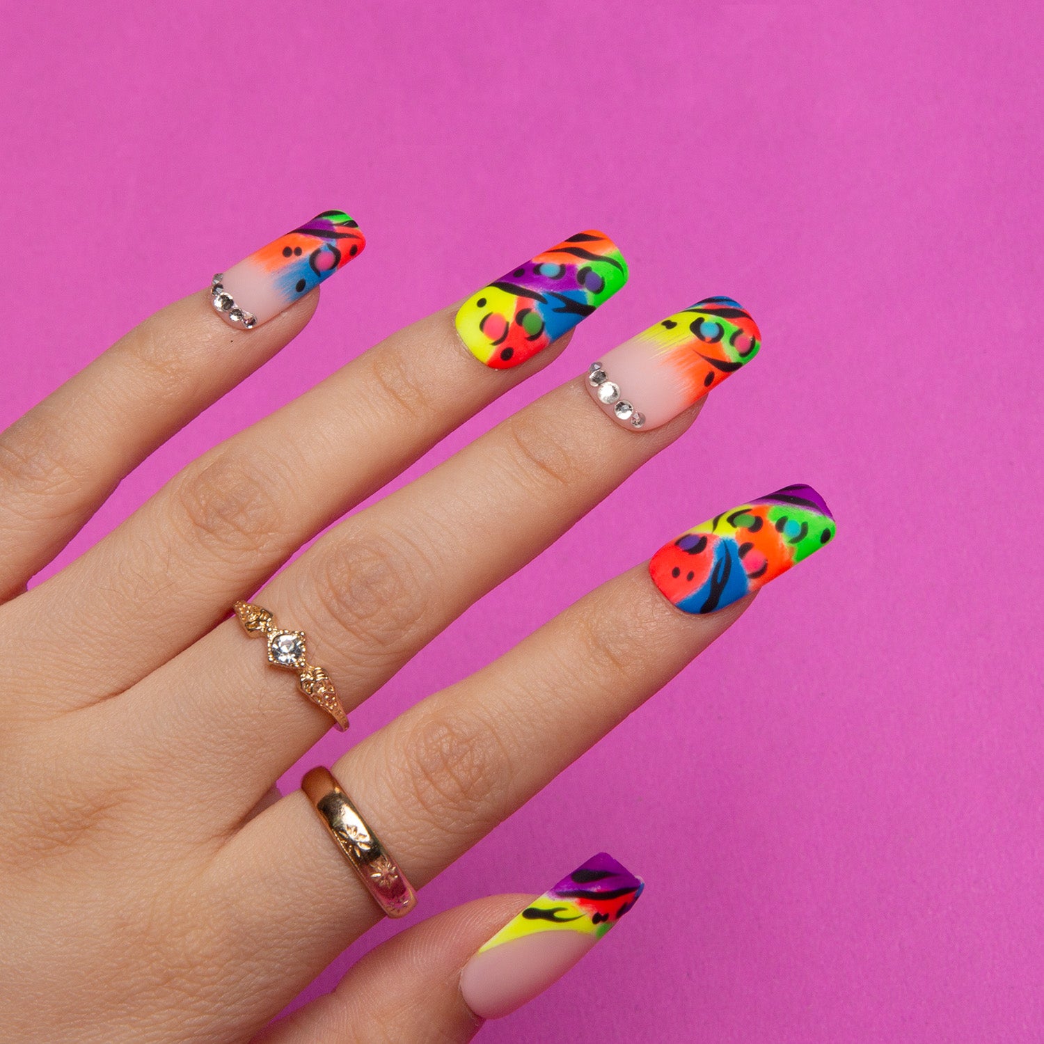 Colorful square press-on nails with bright French tips, vibrant leopard prints, and silver rhinestones against a pink background
