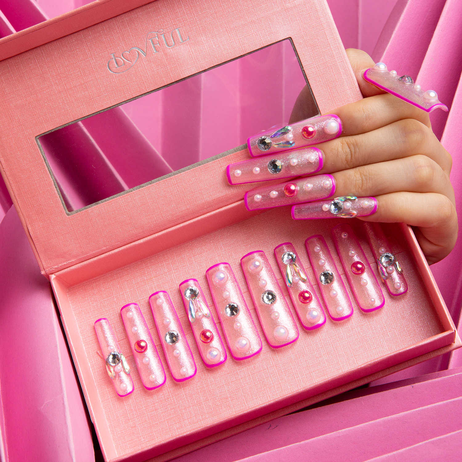 A hand holding a box of pink press on nails