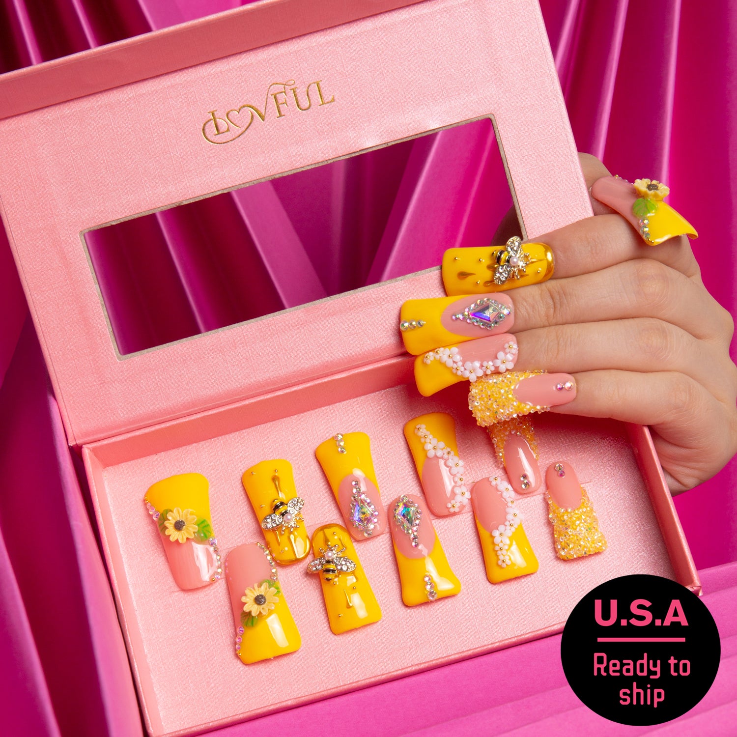 Set of bright yellow press-on nails in a pink box, featuring sunflower patterns, bee accents, and rhinestones. Hand holding one nail, with 'U.S.A Ready to ship' text sticker.
