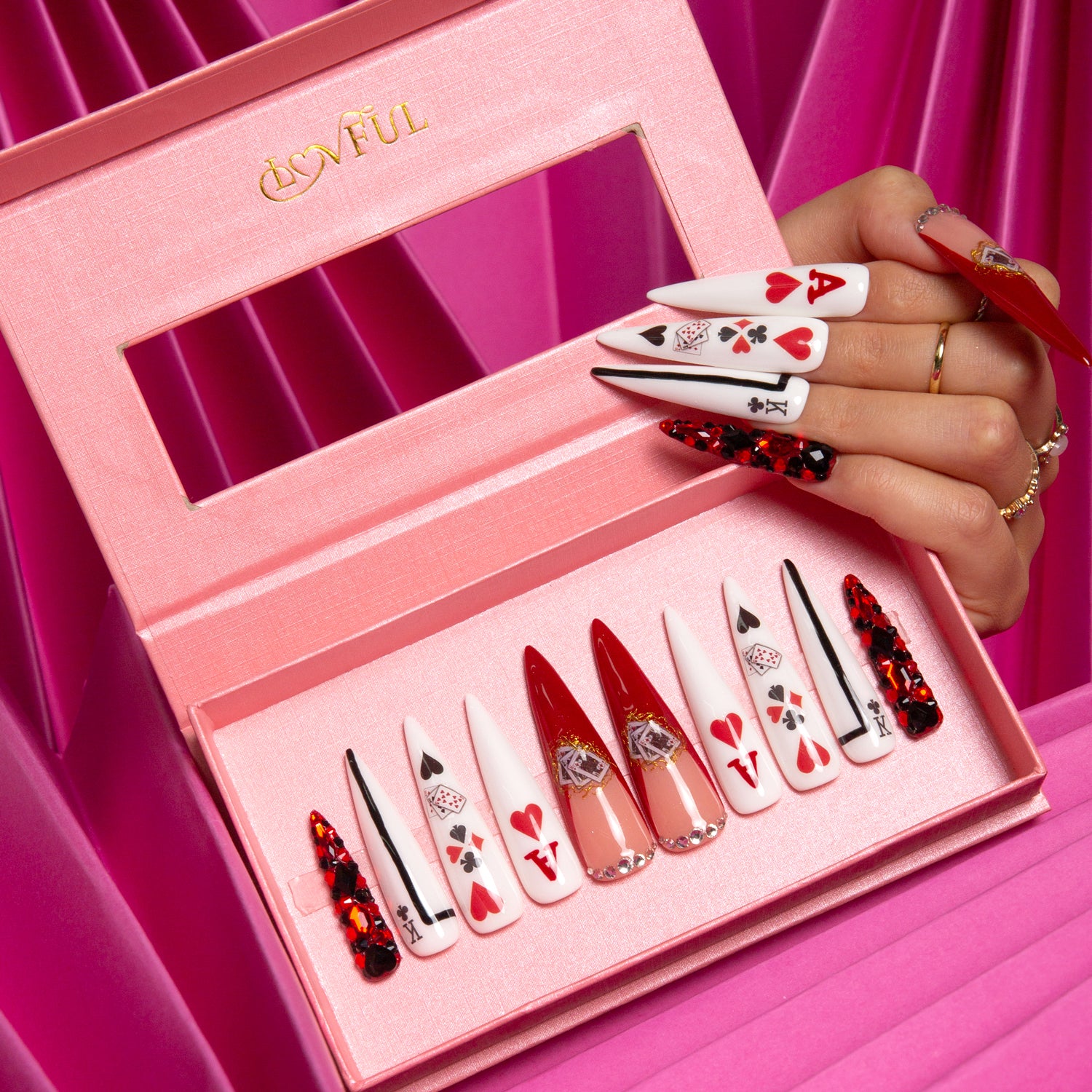 Poker Queen stiletto press-on nails by Lovful in a pink box. Each nail features red and white playing card designs including hearts and spades. A hand showcases some nails. The pink box has Lovful logo.