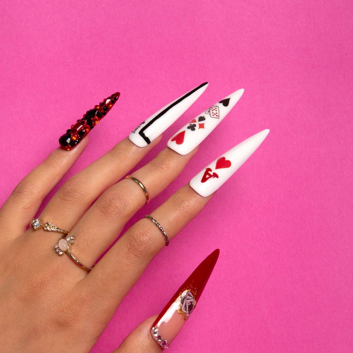 Hand with Poker Queen stiletto press-on nails featuring red and white designs including playing cards, card suits, and hearts on a pink background.