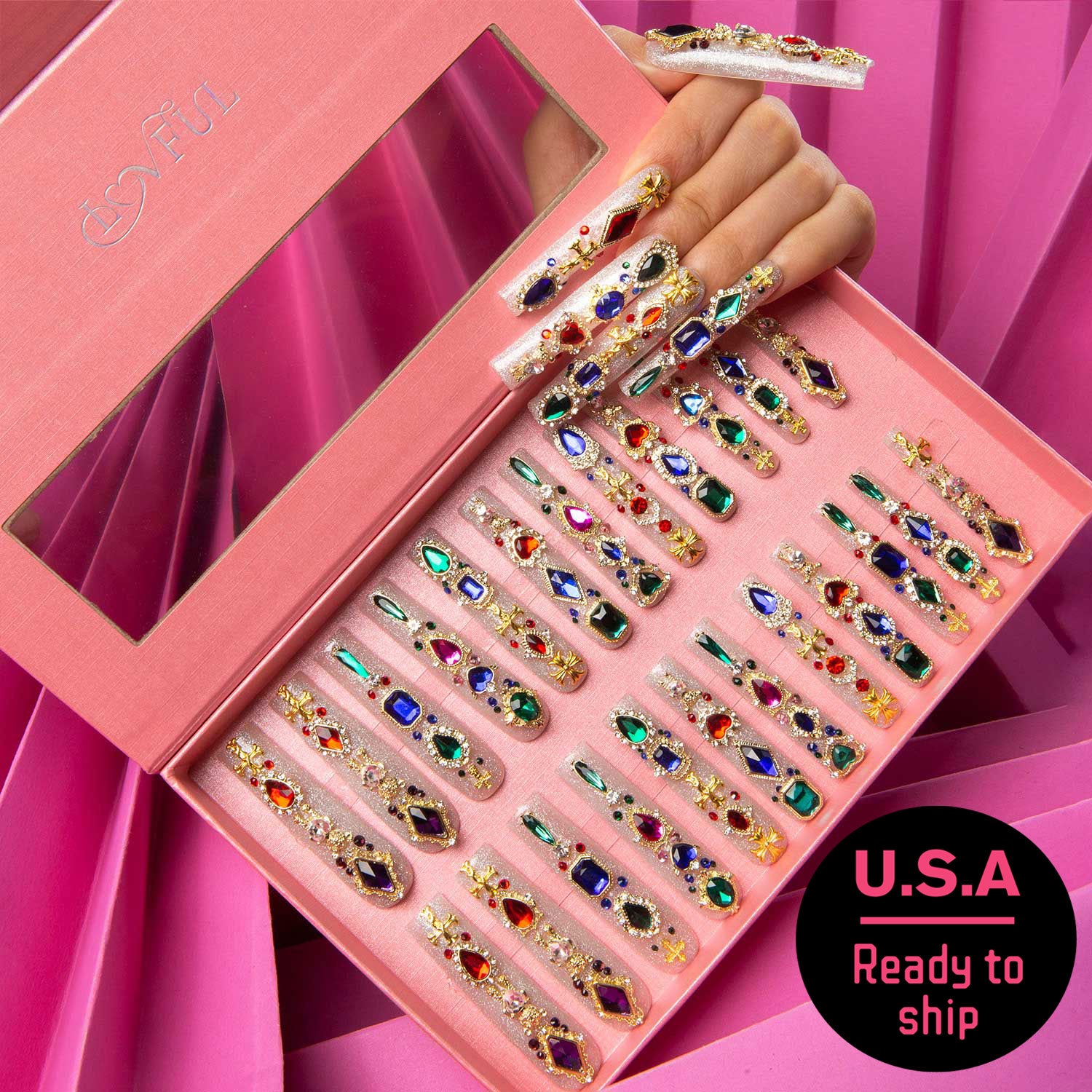 Decorative pink box containing 24 press-on nails with colorful gems and glitter. Hand displaying some nails. Label reads 'U.S.A Ready to ship'.