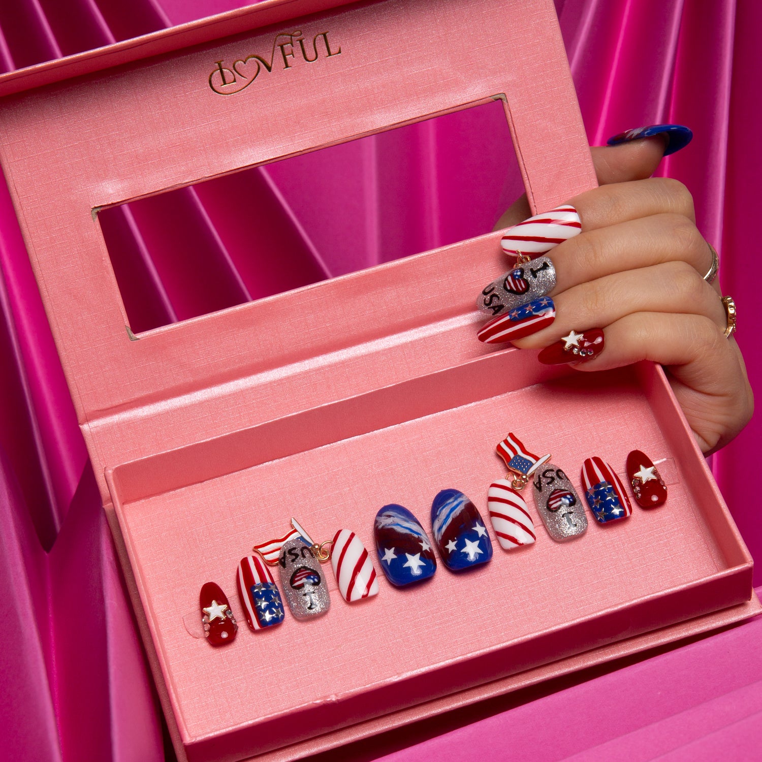 Hand displaying American Dream press-on nail set from Lovful in a pink box. The nails feature American flag designs with red, white, blue colors, stars, stripes and USA-themed art, perfect for National Day and Independence Day celebrations.