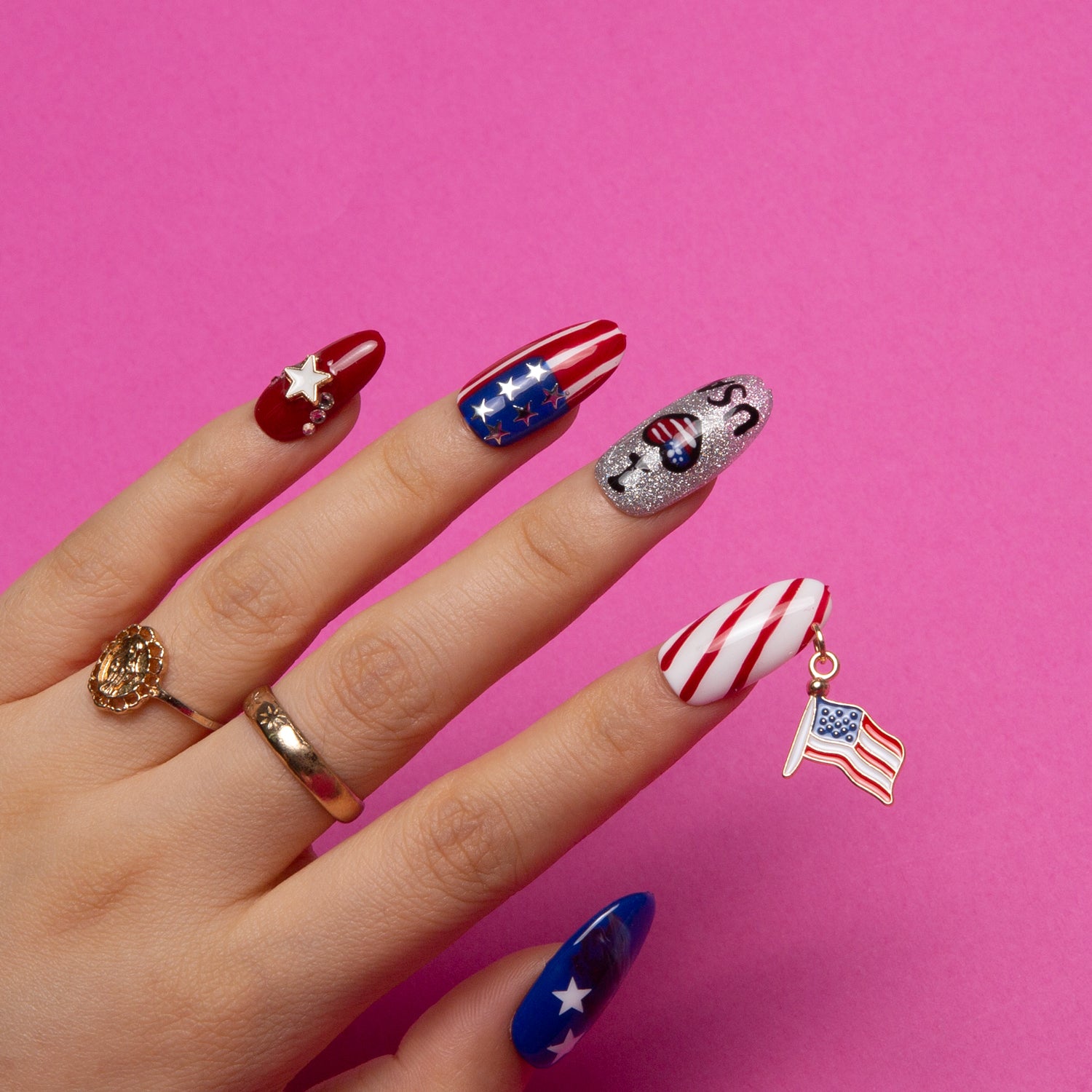 Hand with press-on nails in patriotic American theme, featuring red and white stripes, blue with stars, silver glitter with 'USA' text, and an American flag charm. Perfect for Independence Day celebrations and July 4th parties.