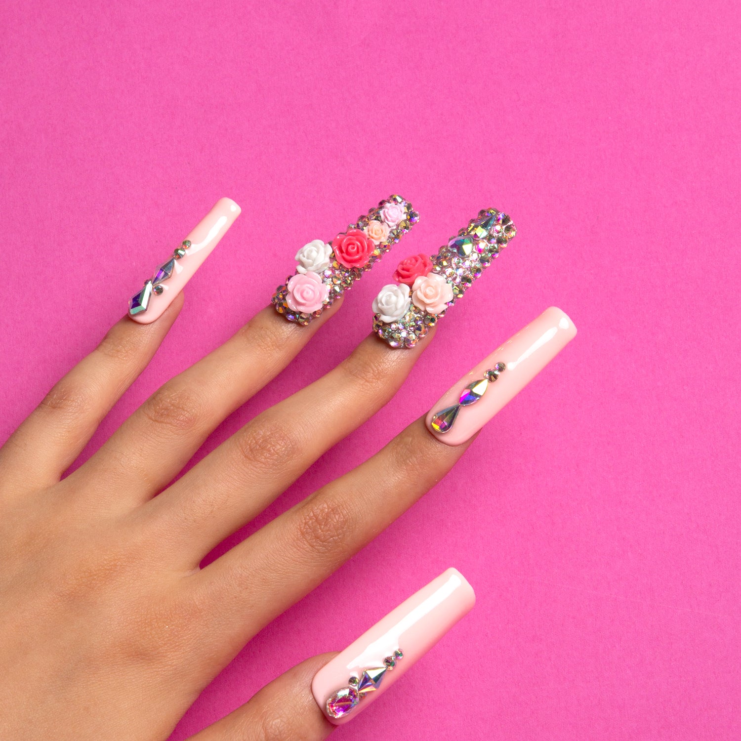 Hand with long square-shaped pink press-on acrylic nails featuring pink and white rose designs and rhinestones