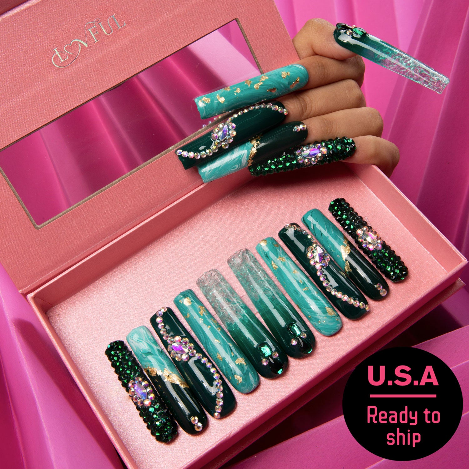 Emerald Envy square-shaped press-on nails in various shades of green with intricate gold designs and embellishments inside pink packaging box. The nails feature sparkling accents and gemstone decorations, capturing the essence of nature's splendor. U.S.A. Ready to ship.