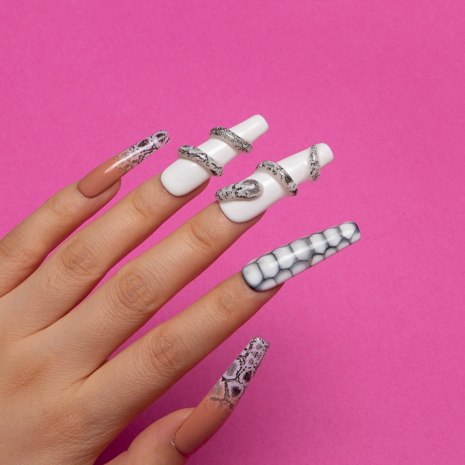 Coffin-shaped Sahara press-on nails with a white base, sand effect, and snake designs on a hand against a pink background.