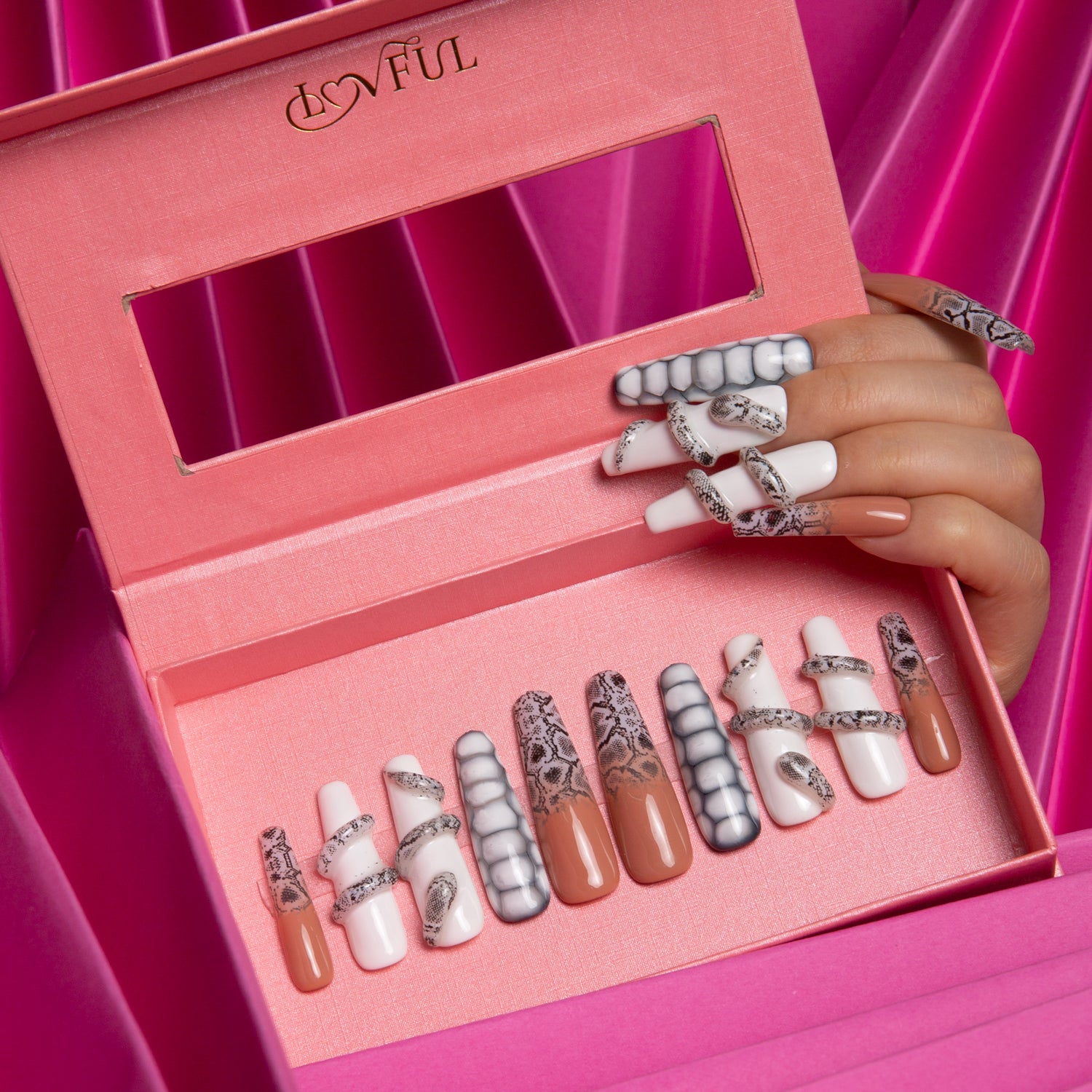 Lovful press-on nail set 'Sahara' with a combination of pure white base, subtle sand effect, and intricate snake designs displayed in a pink box with a hand showing the nails applied, against a pink, silky fabric background.