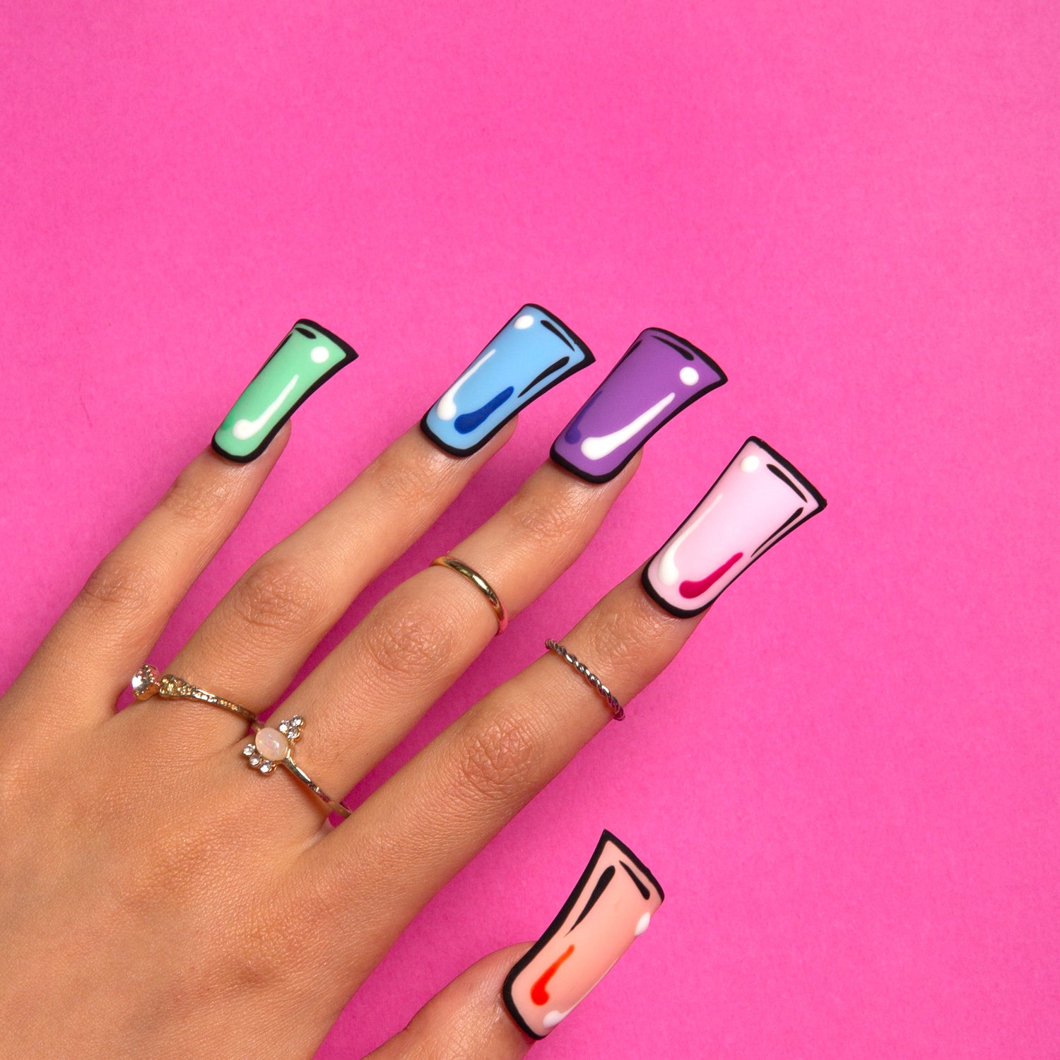 Hand with colorful pop art press-on acrylic nails on a pink background. Nails include green, blue, purple, pink, and peach with black borders.